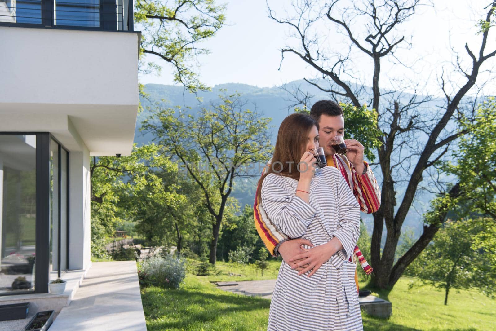 Young beautiful couple in bathrobes are enjoying morning coffee in front of their luxury home villa