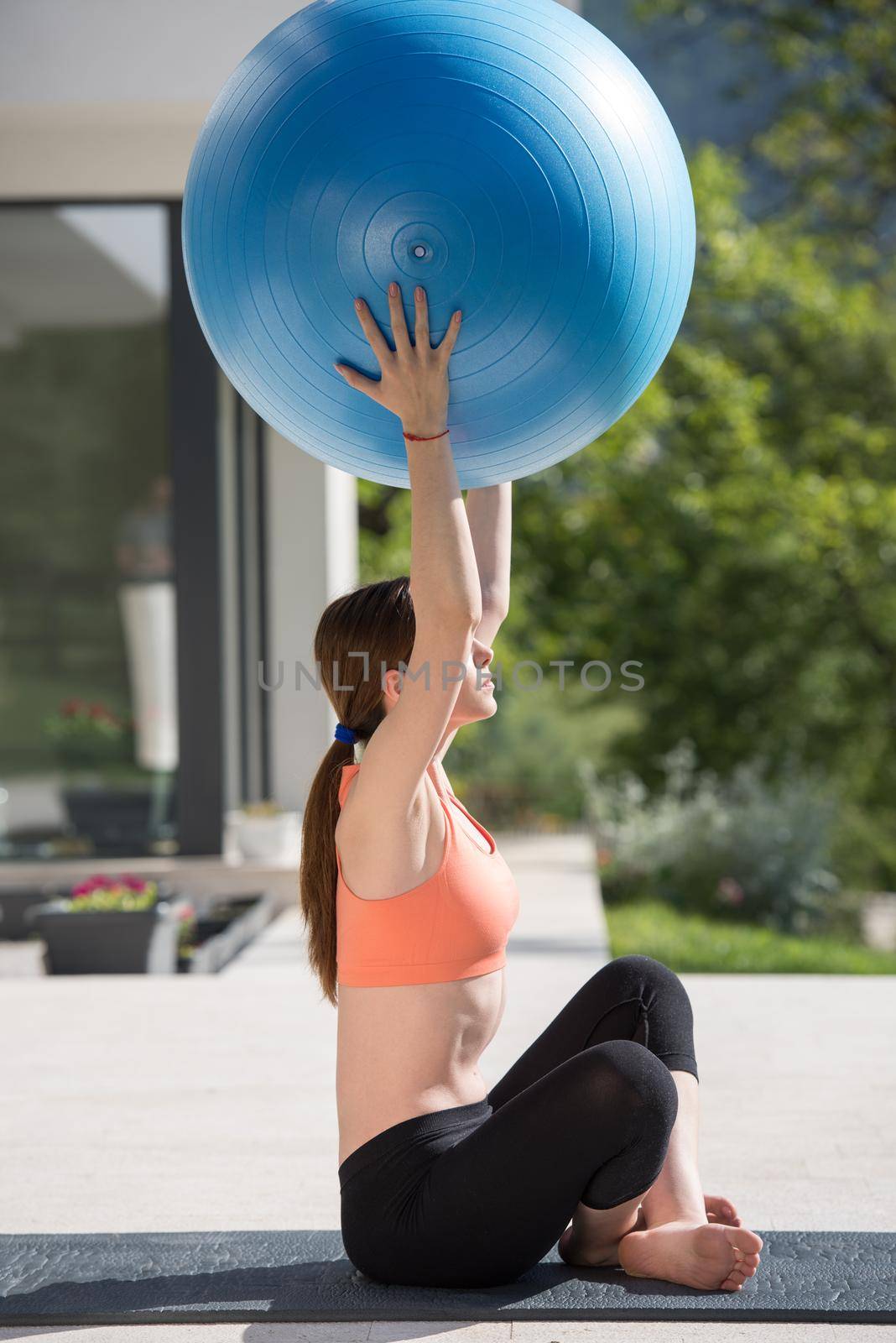 young beautiful woman doing exercise with pilates ball in front of her luxury home villa