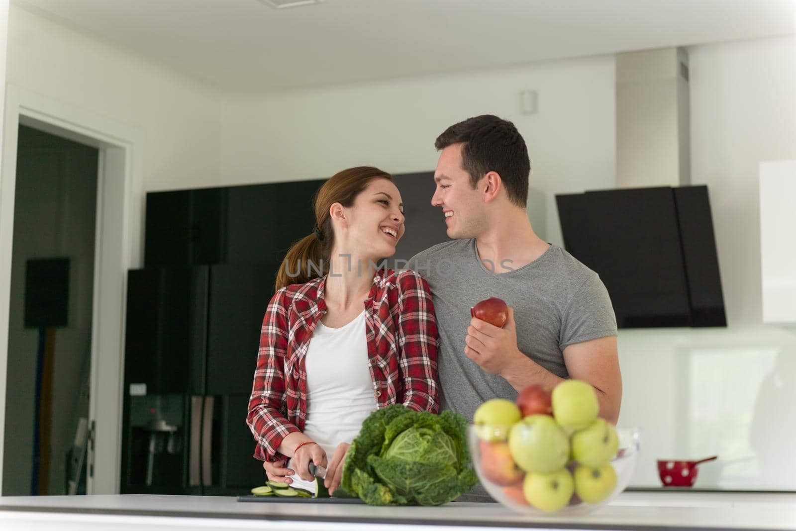 Young handsome couple in the kitchen  beautiful woman preparing a salad while the man eating an apple