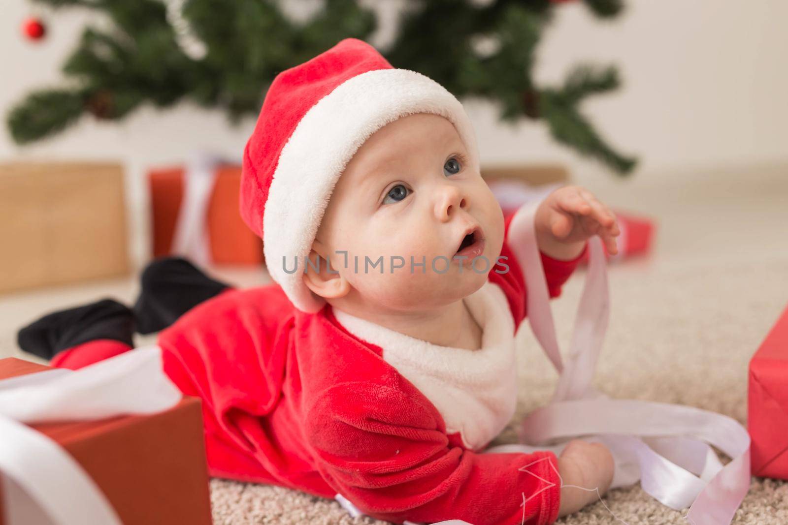 Beautiful little baby celebrates Christmas. New Year's holidays. Baby in a Christmas costume and in santa hat and gift box.