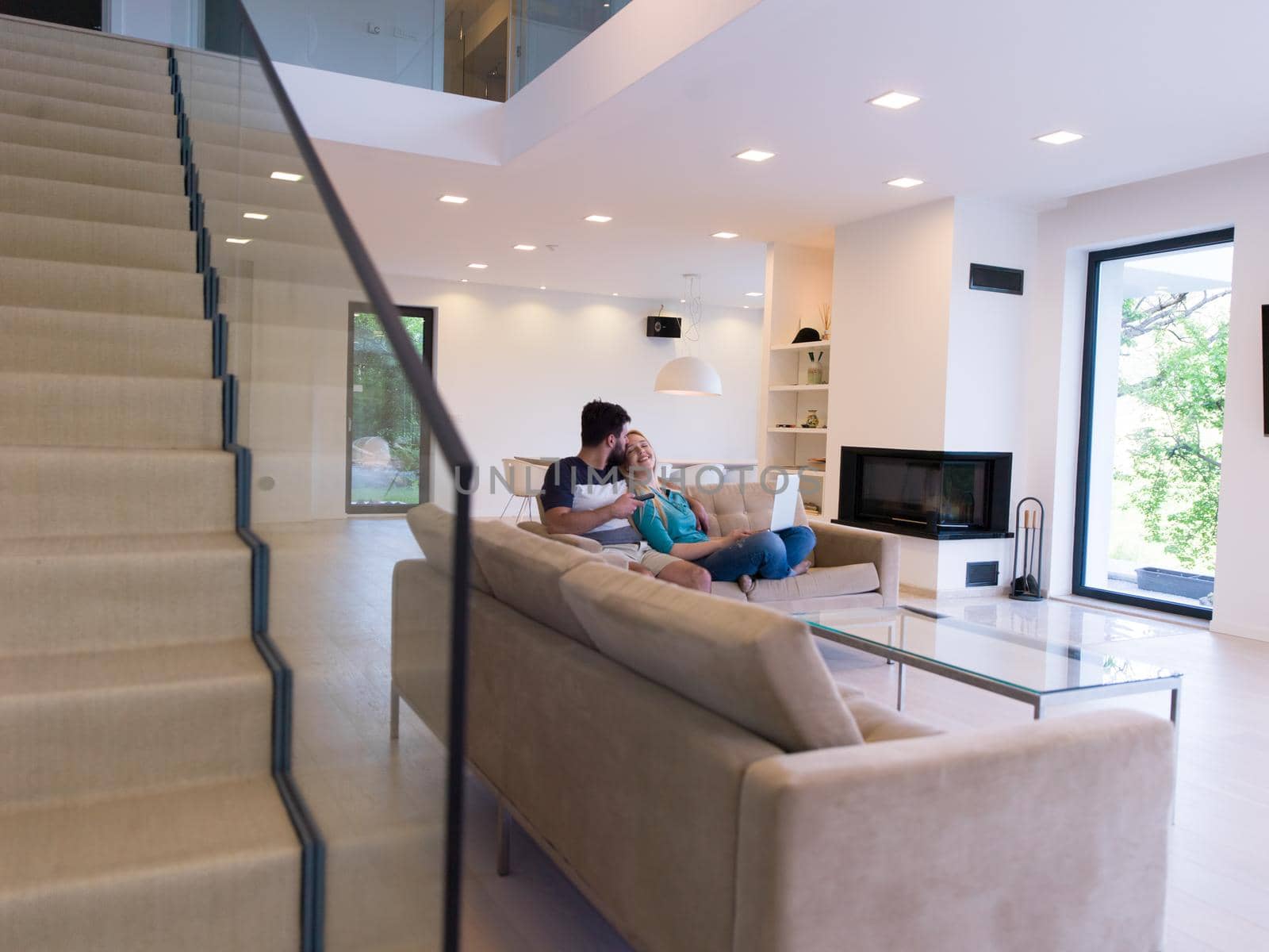 Young couple relaxes on the sofa in the luxury living room, using a laptop and remote control