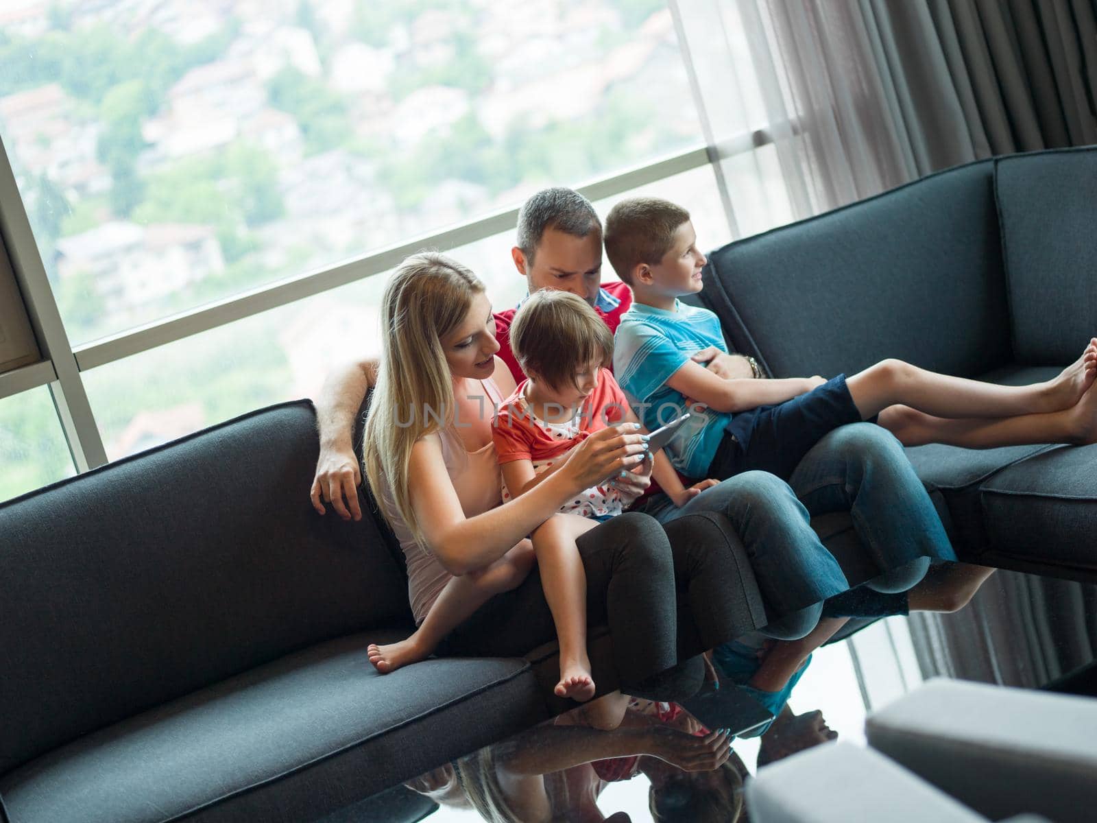 Happy Young Family Playing Together with tablet at home sitting on the sofa