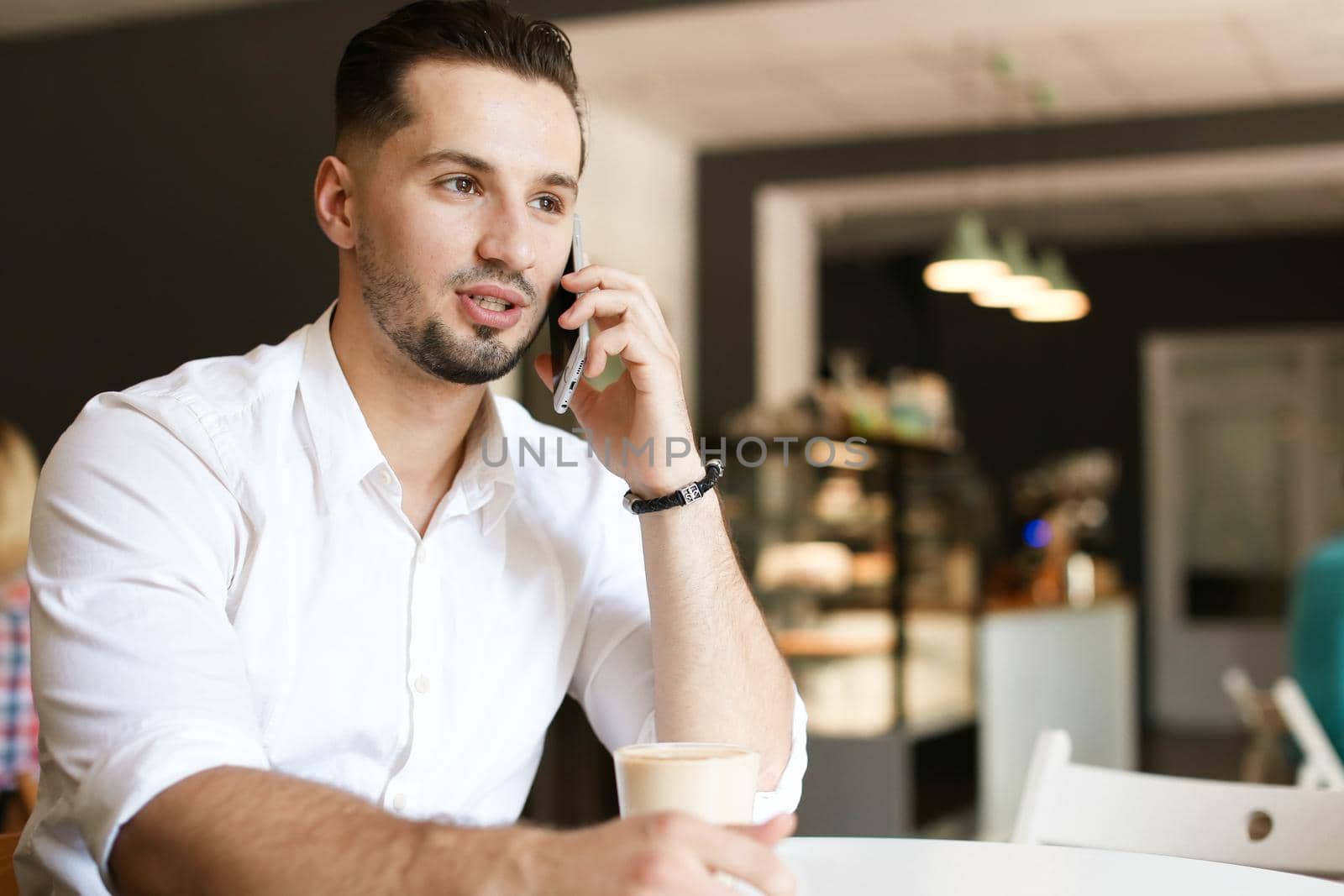 Young caucasian businessman talking by smartphone at cafe. Concept of modern technology and businessperson.