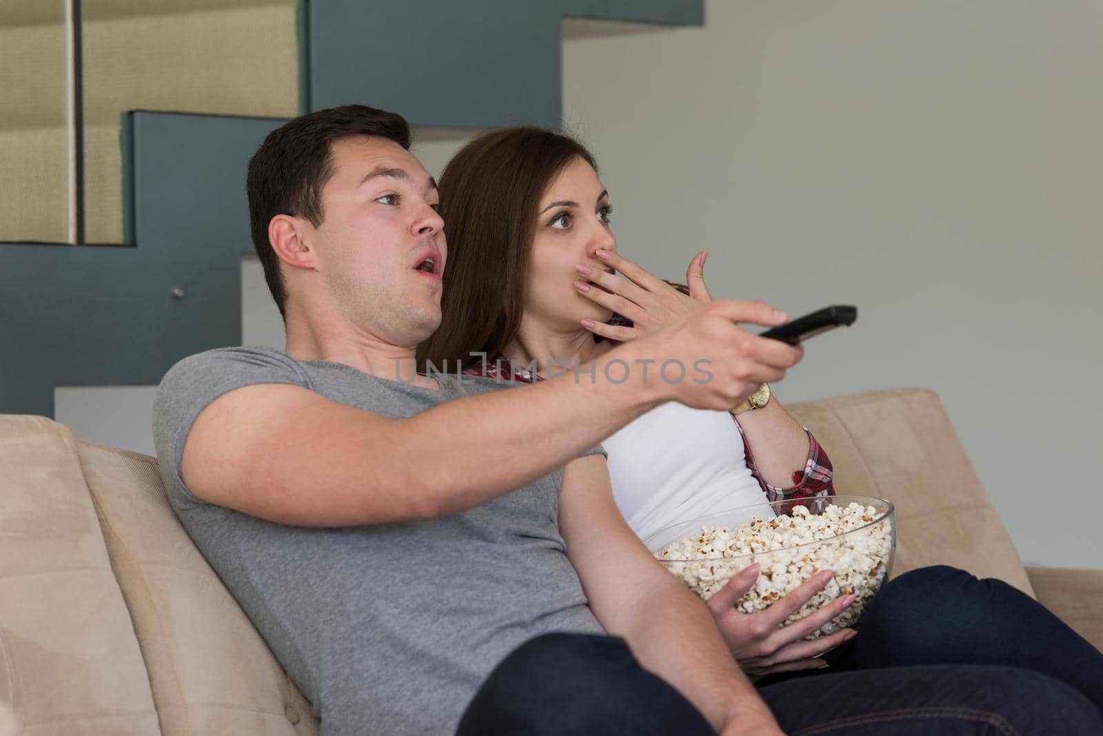 young handsome couple enjoying free time watching television with popcorn in their luxury home villa