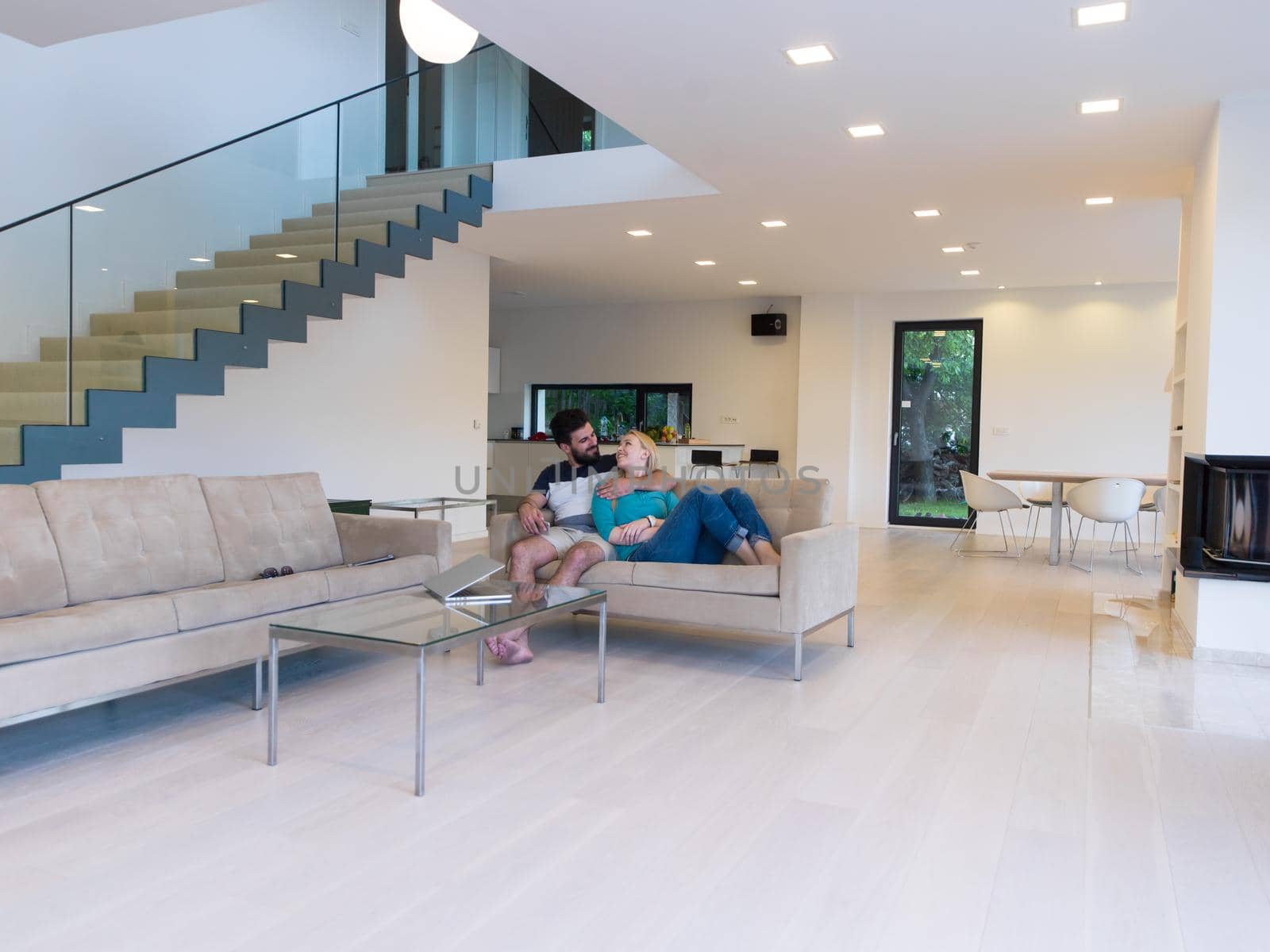 Young couple relaxes on the sofa in the luxury living room, using a laptop and remote control