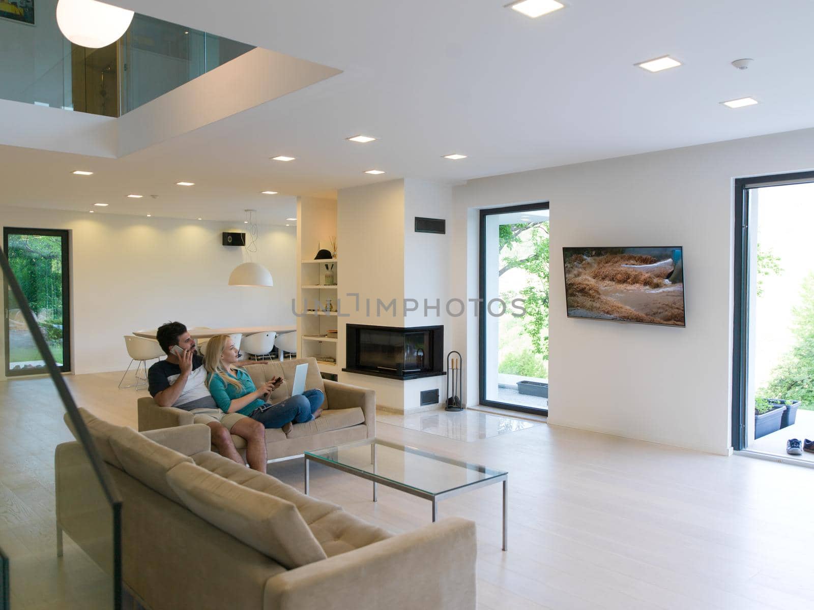 Young couple relaxes on the sofa in the luxury living room, using a laptop and remote control