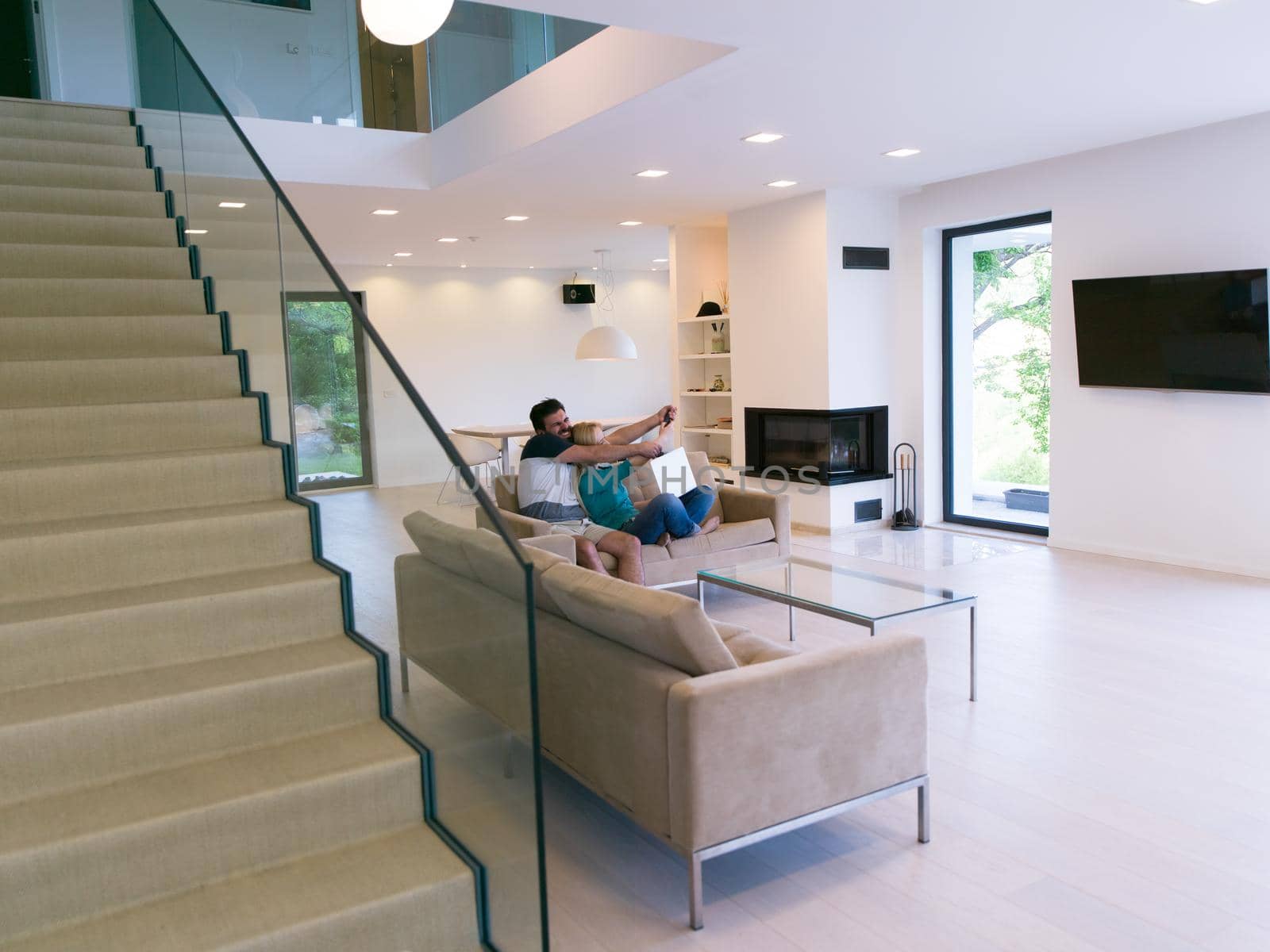 Young couple relaxes on the sofa in the luxury living room, using a laptop and remote control