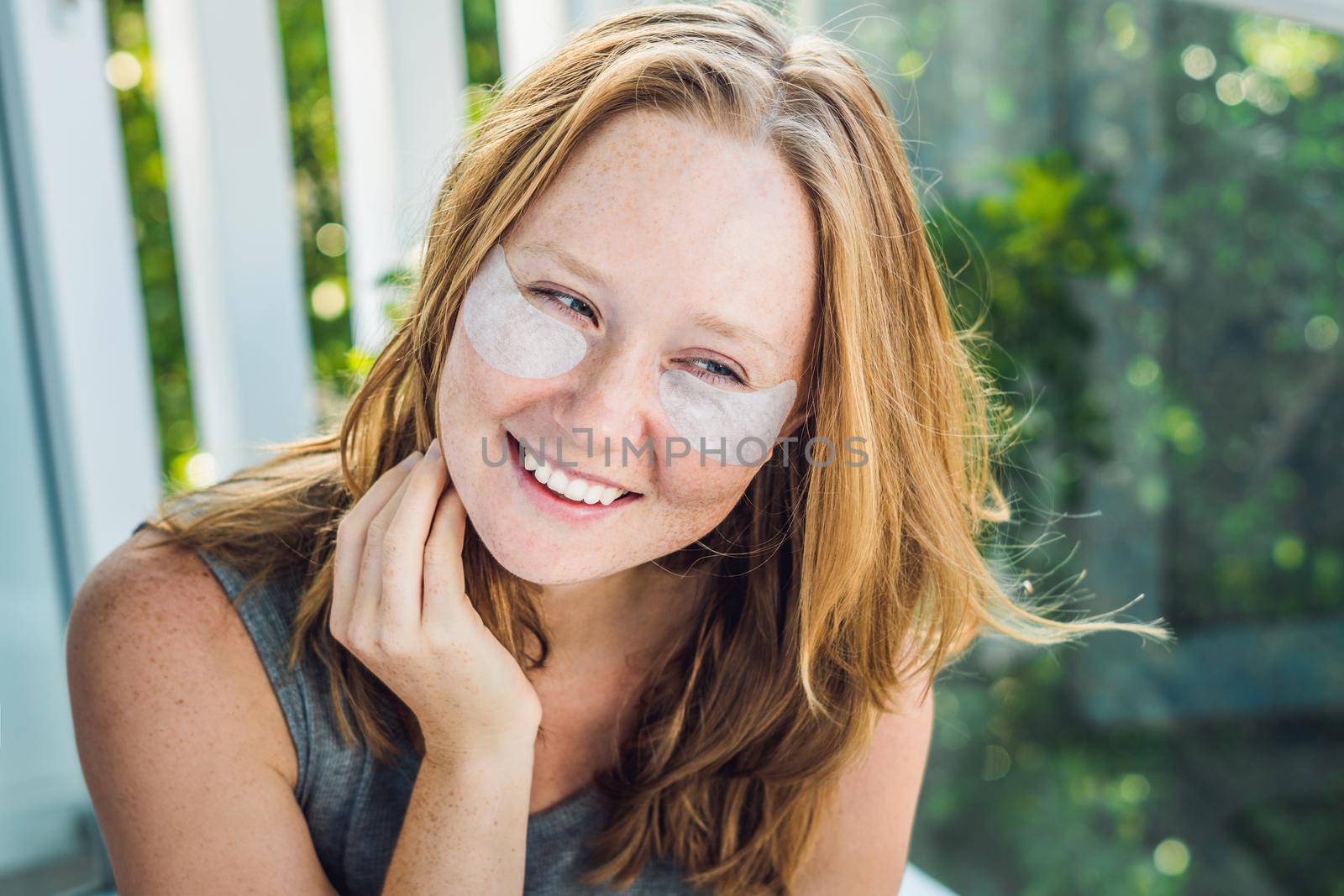 Portrait of Beauty Red-haired woman with eye patches showing an effect of perfect skin. Spa Girl.