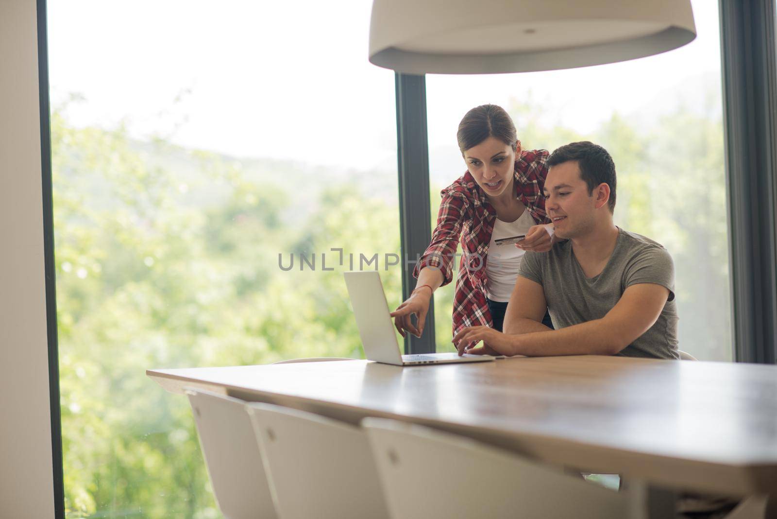 happy young couple buying online using laptop a computer and a credit card in their luxury home villa