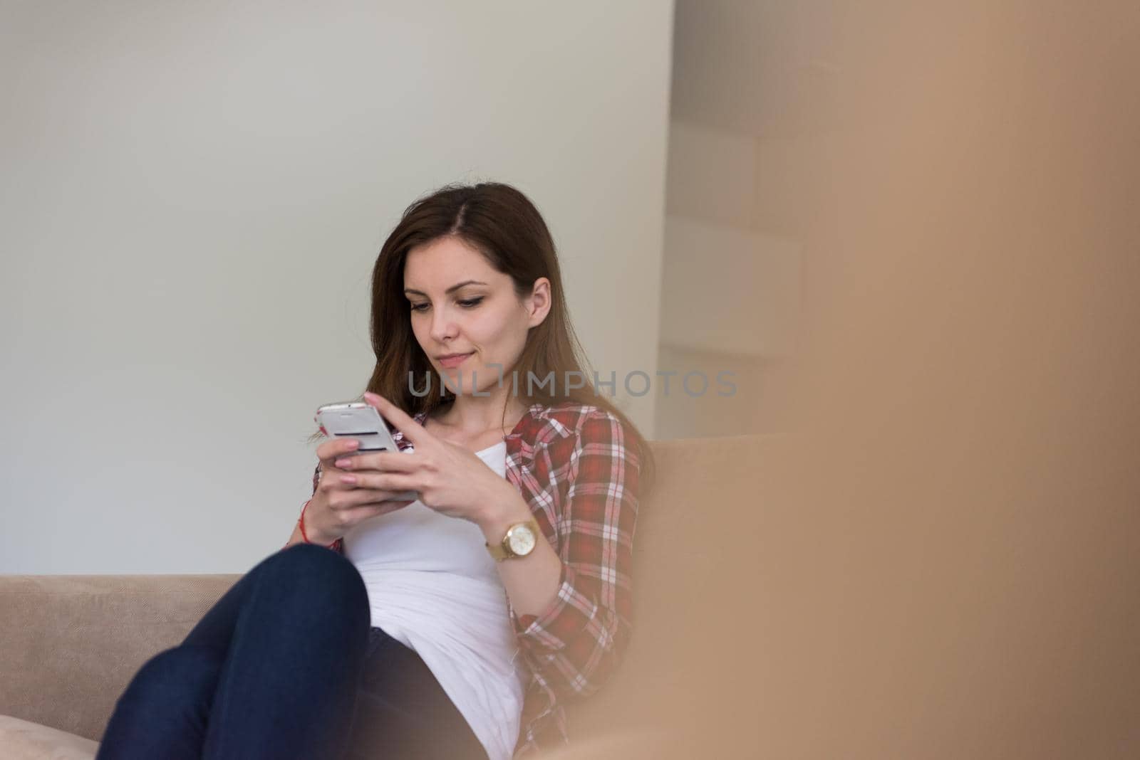 young happy woman sitting on sofa and using mobile phone at luxury home