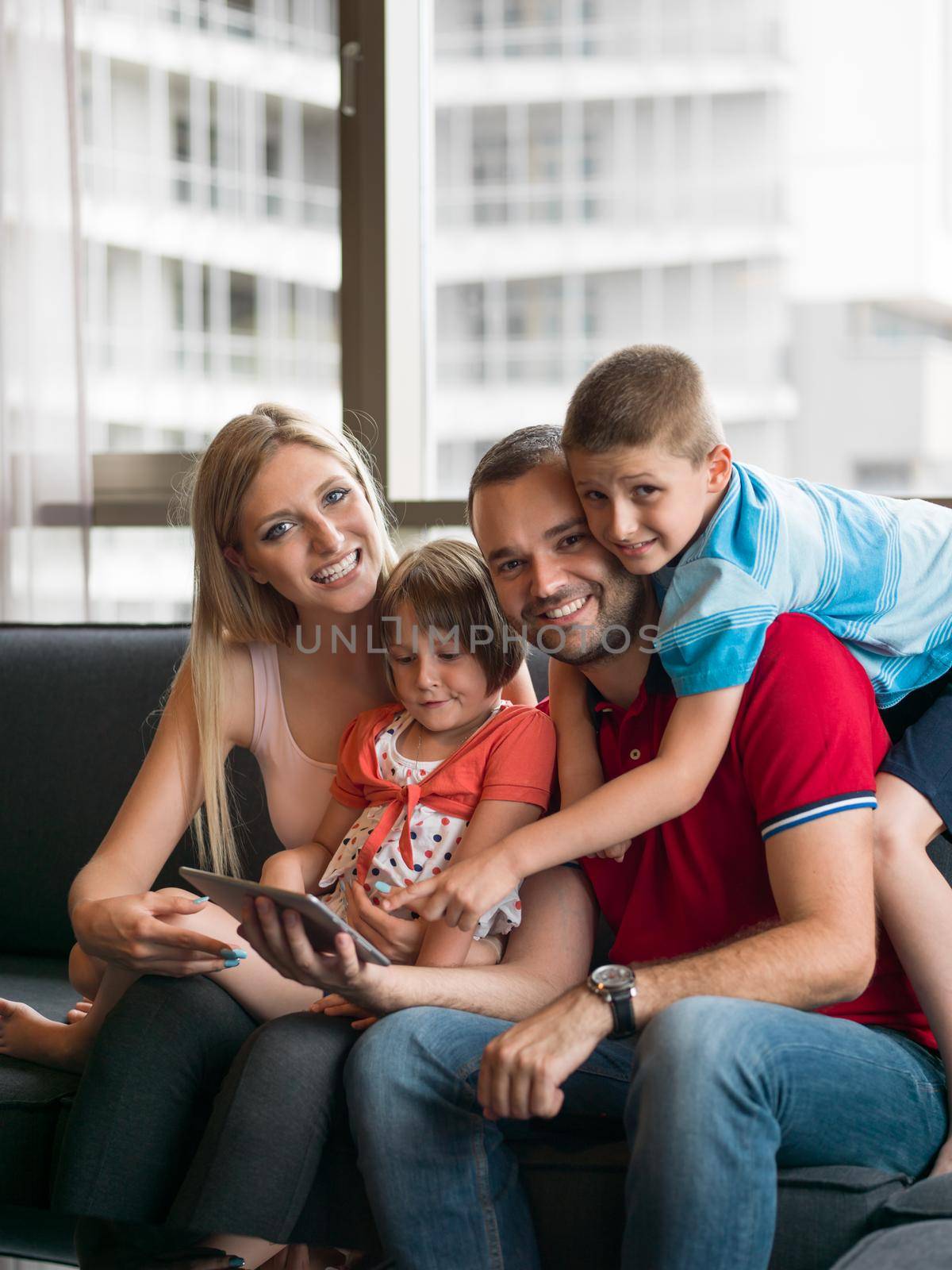 Happy Young Family Playing Together with tablet at home sitting on the sofa