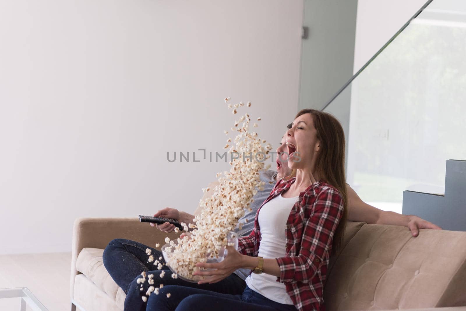 young handsome couple enjoying free time watching television with popcorn in their luxury home villa