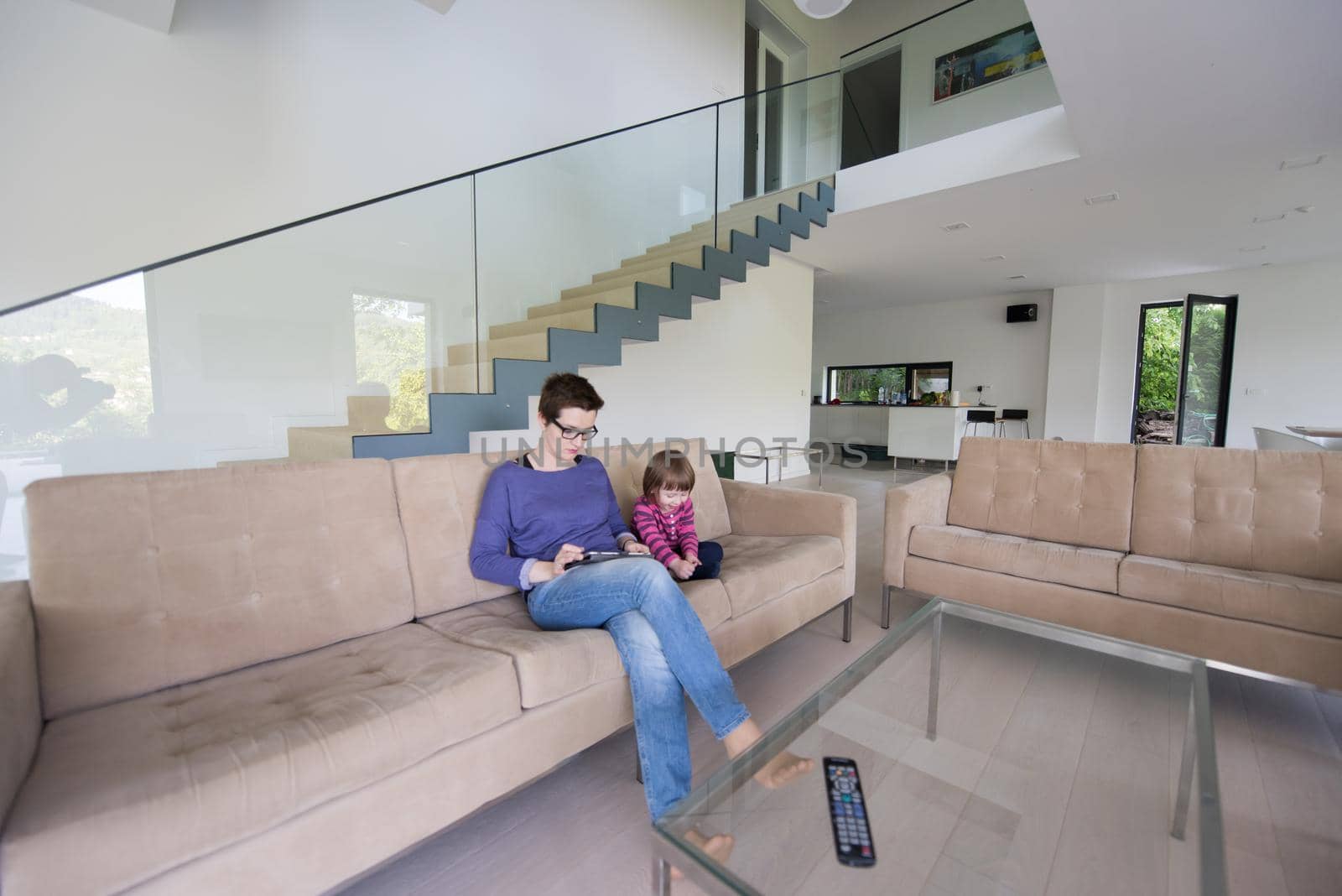 Beautiful young mother and her cute little daughter are using a tablet and smiling, sitting on sofa at home