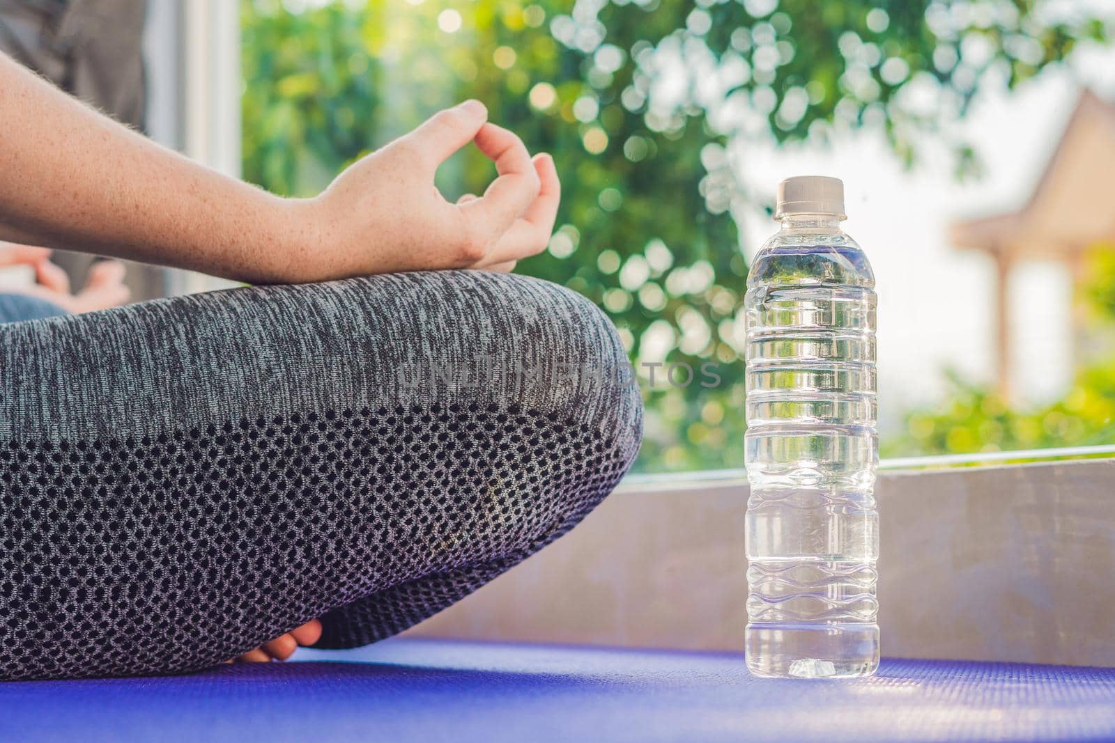 hand of a woman meditating in a yoga pose on a rug for yoga and a bottle of water.