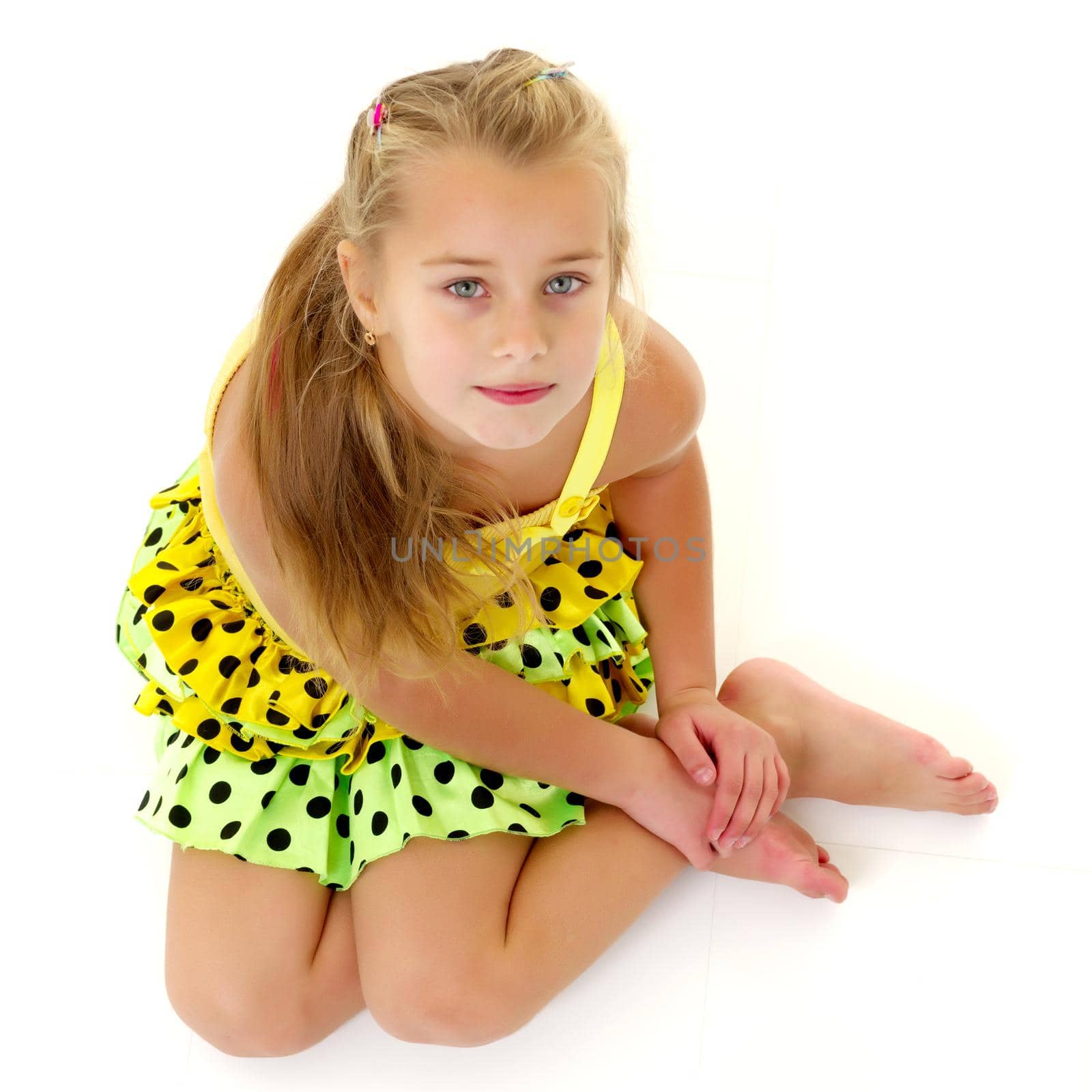 Beautiful little girl is sitting on the floor in the studio. The concept of a happy childhood, beauty and fashion. Isolated on white background.