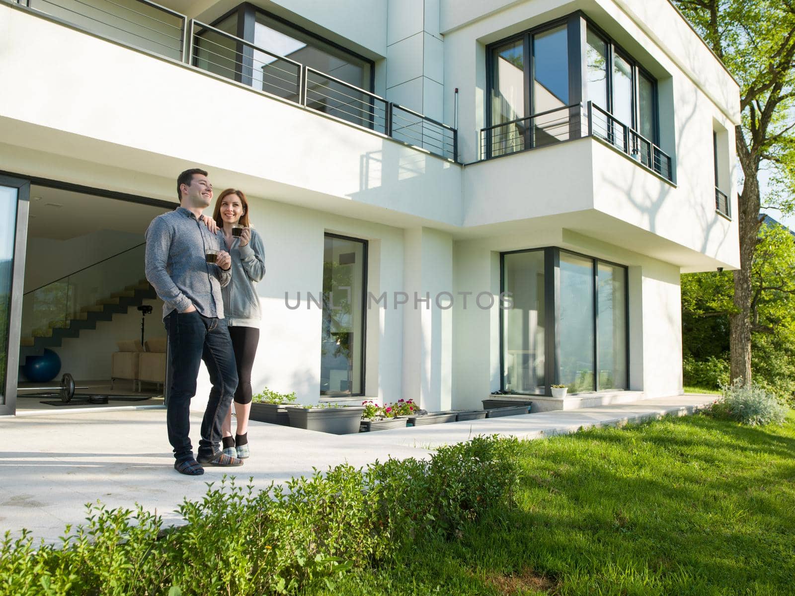 young beautiful handsome couple enjoying morning coffee in front of their luxury home villa