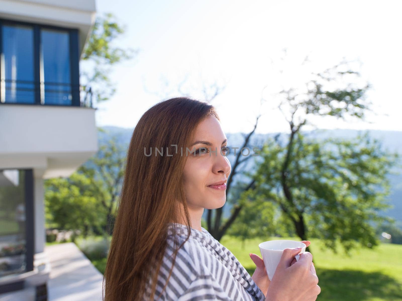 young beautiful woman in a bathrobe enjoying morning coffee in front of her luxury home villa