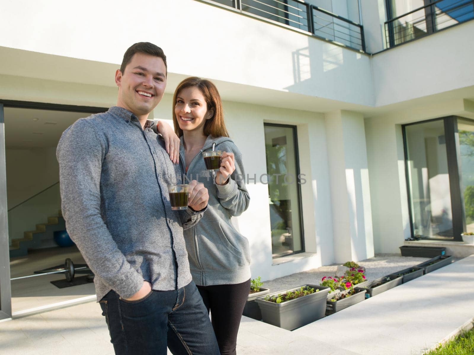 young beautiful handsome couple enjoying morning coffee in front of their luxury home villa