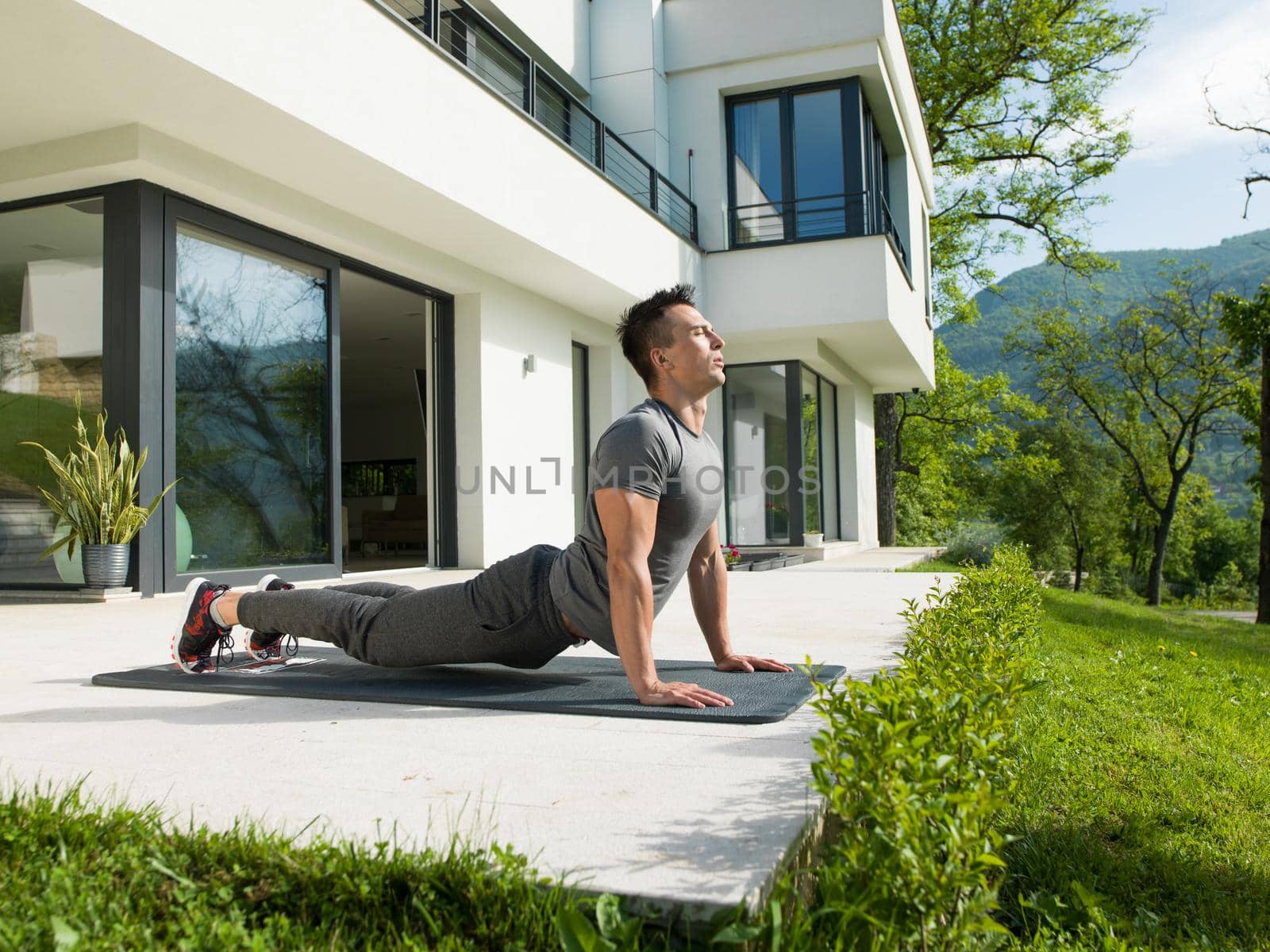 young handsome man doing morning yoga exercises in front of his luxury home villa