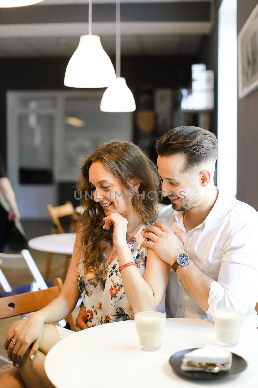 Young handsome man hugging woman at cafe, ,sitting near cups of coffee. Concept of positive emotions, feelings and resting on lunch.