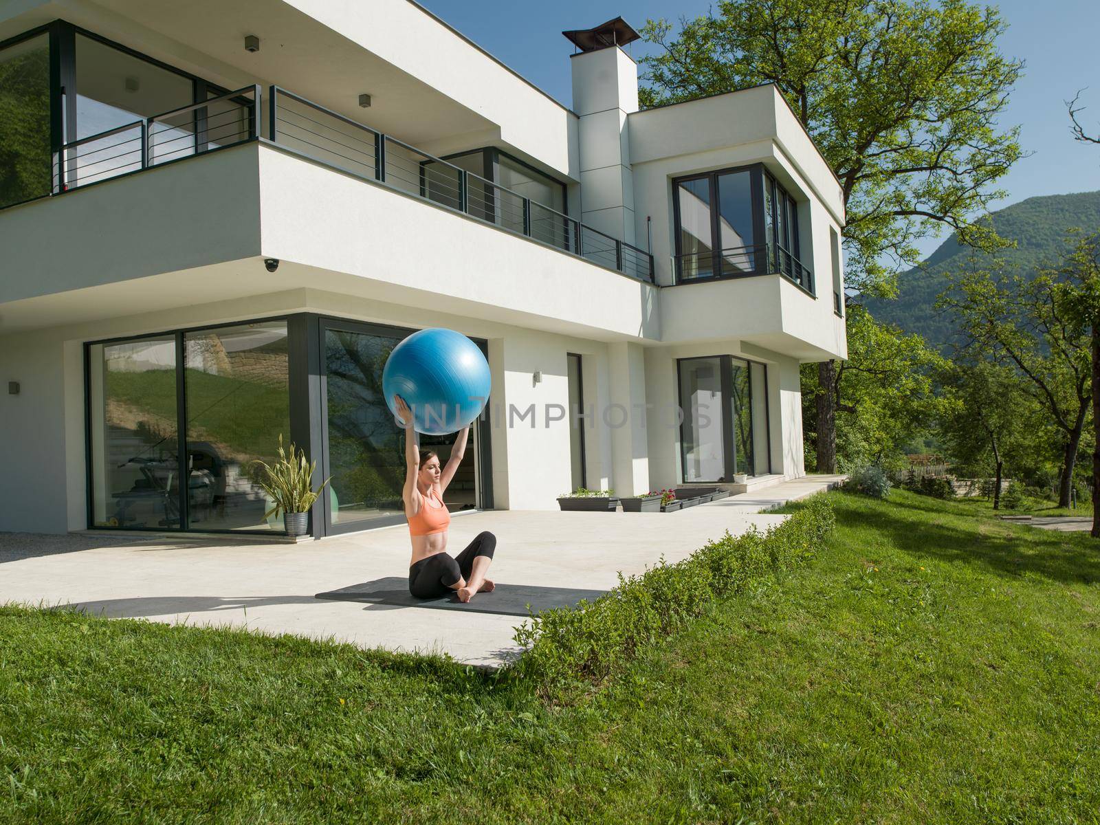 young beautiful woman doing exercise with pilates ball in front of her luxury home villa