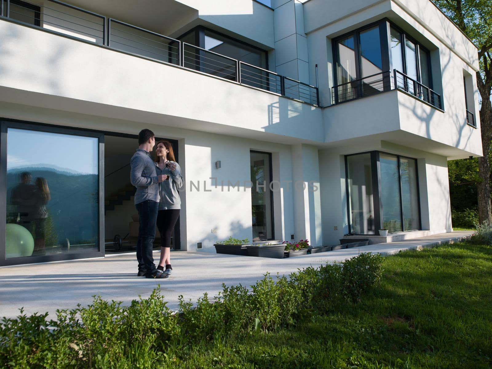 young beautiful handsome couple enjoying morning coffee in front of their luxury home villa