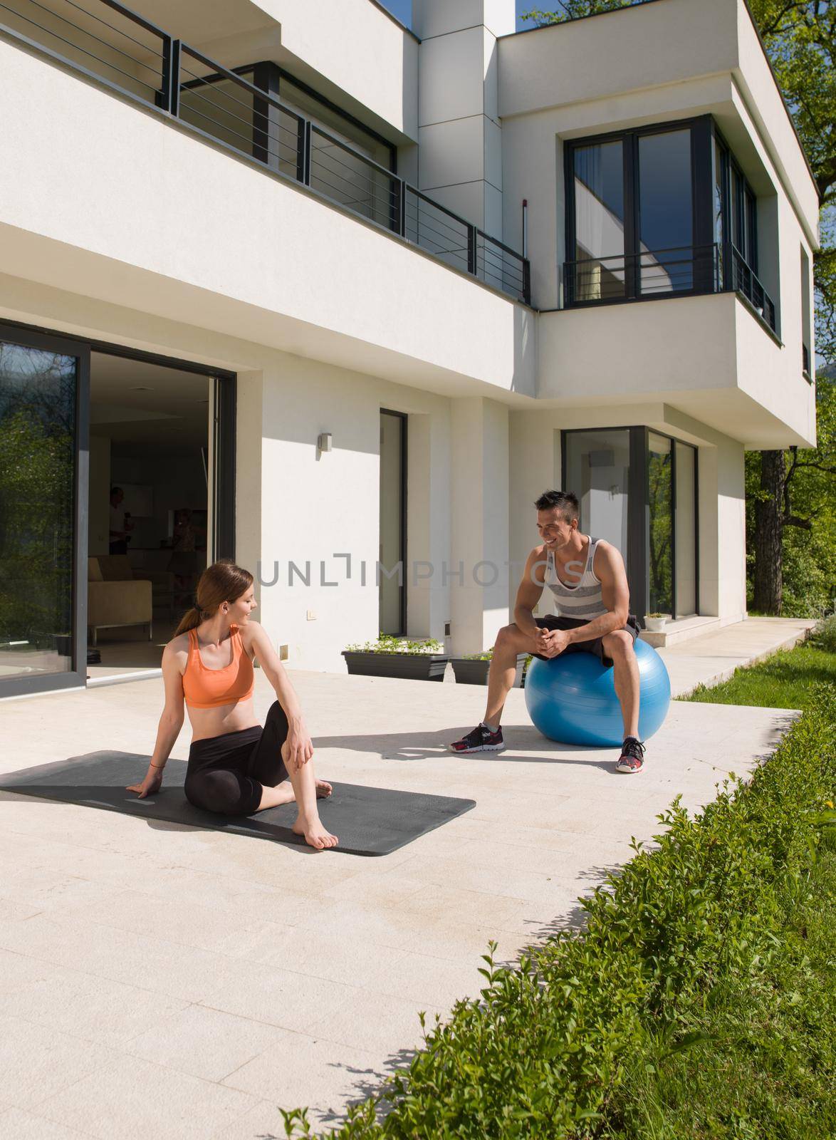 young beautiful woman and personal trainer doing exercise with pilates ball in front of her luxury home