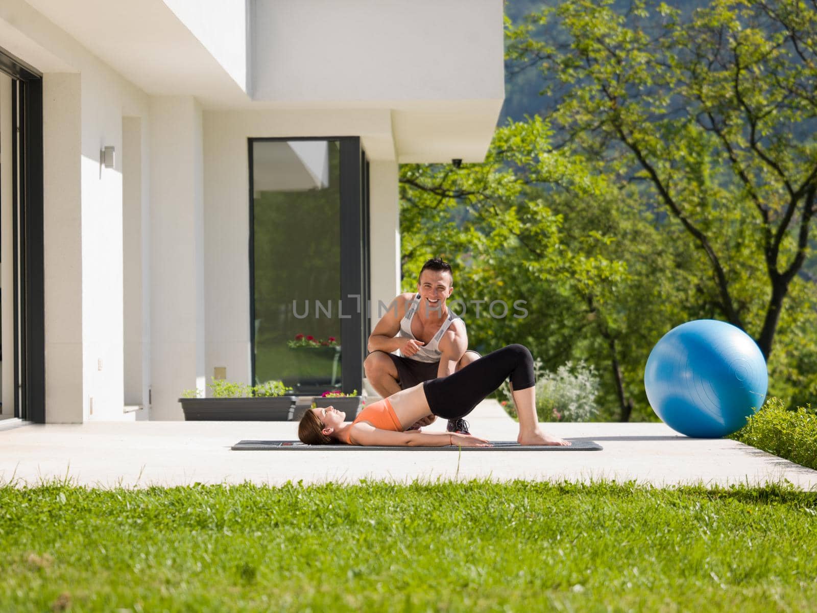 young handsome woman with personal trainer doing morning yoga exercises in front of her luxury home villa