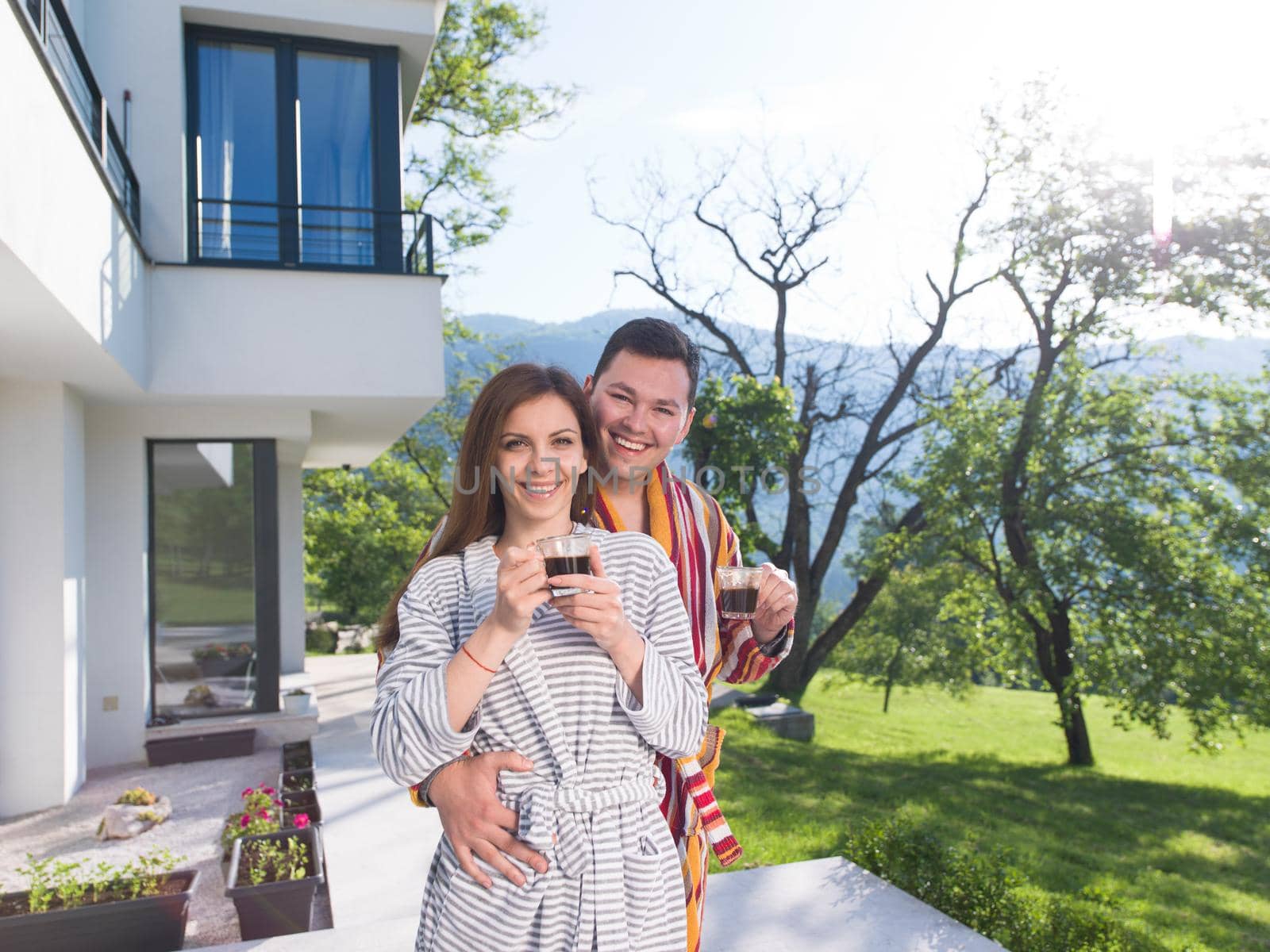 Young beautiful couple in bathrobes are enjoying morning coffee in front of their luxury home villa