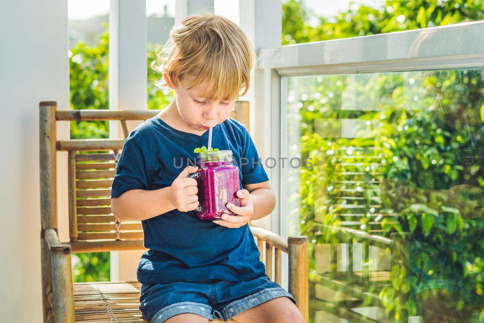 The boy holds smoothies from a dragon fruit with a mint leaf and a drinking straw.