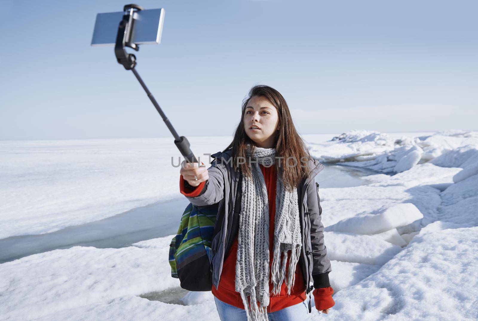 Female traveler outdoors at icy landscape using monopod to make selfie picture by Novic
