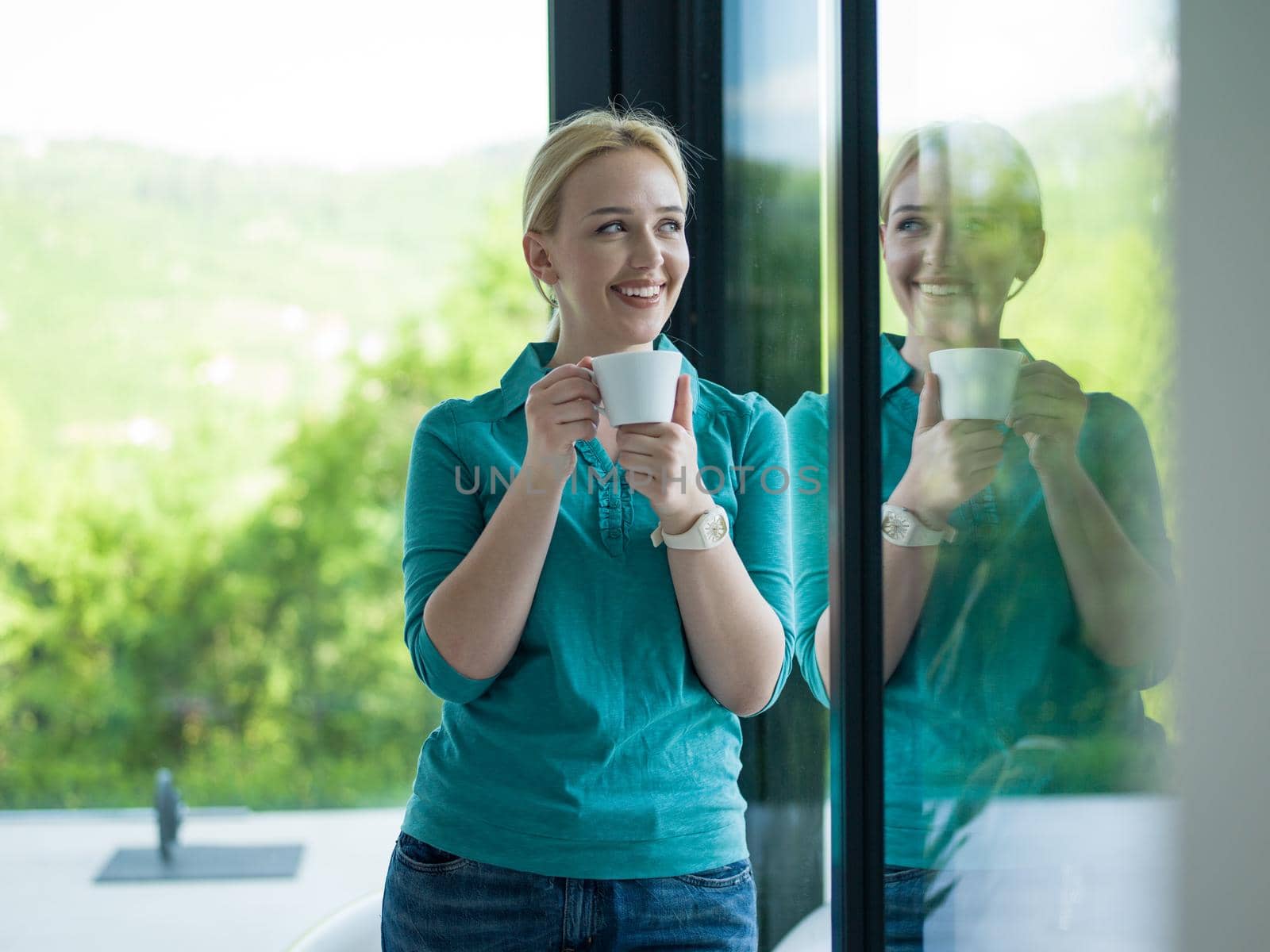 beautiful young woman drinking morning coffee by the window in her home