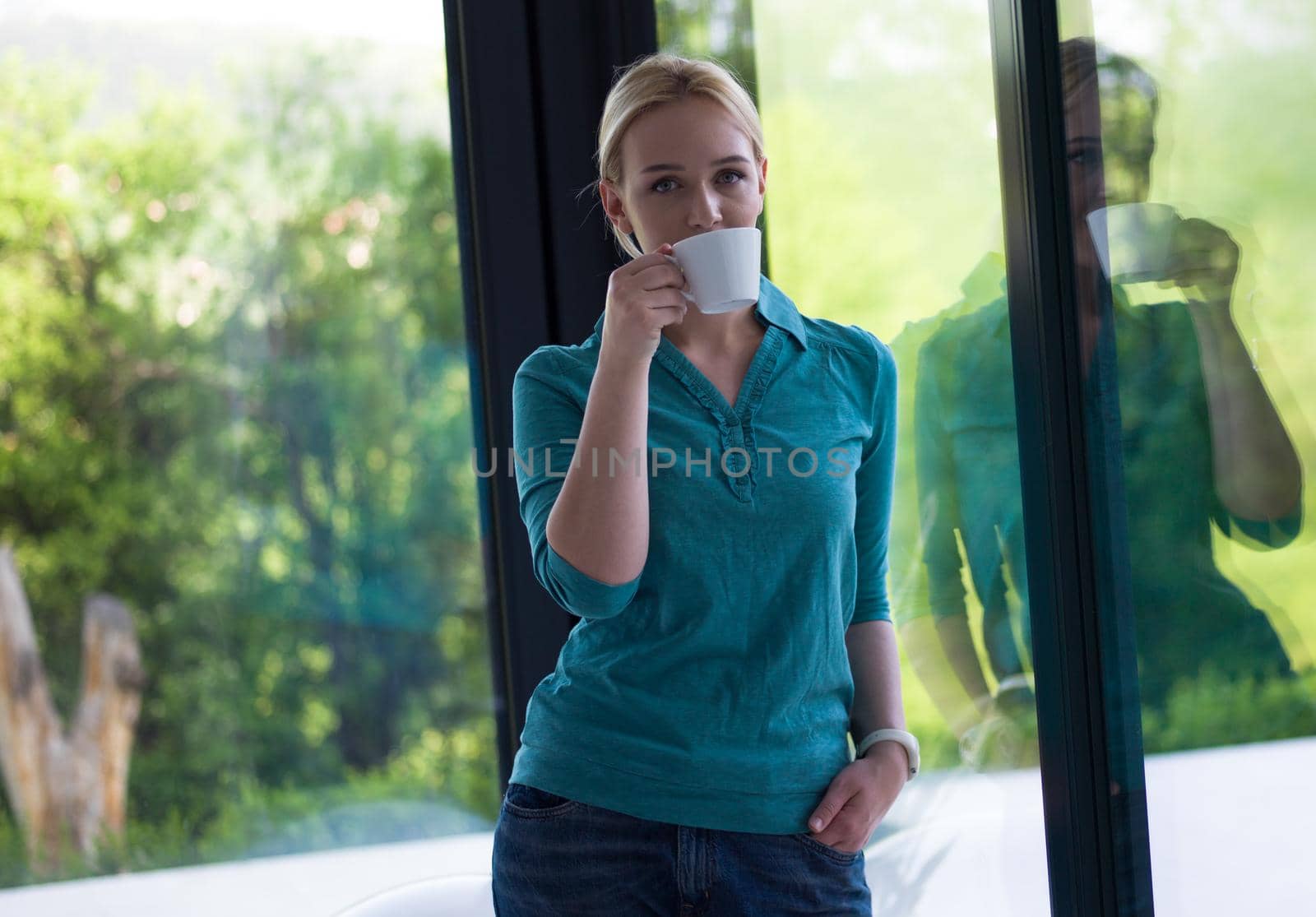 beautiful young woman drinking morning coffee by the window in her home