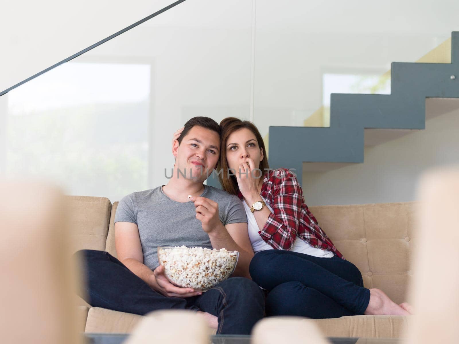 young handsome couple enjoying free time watching television with popcorn in their luxury home villa