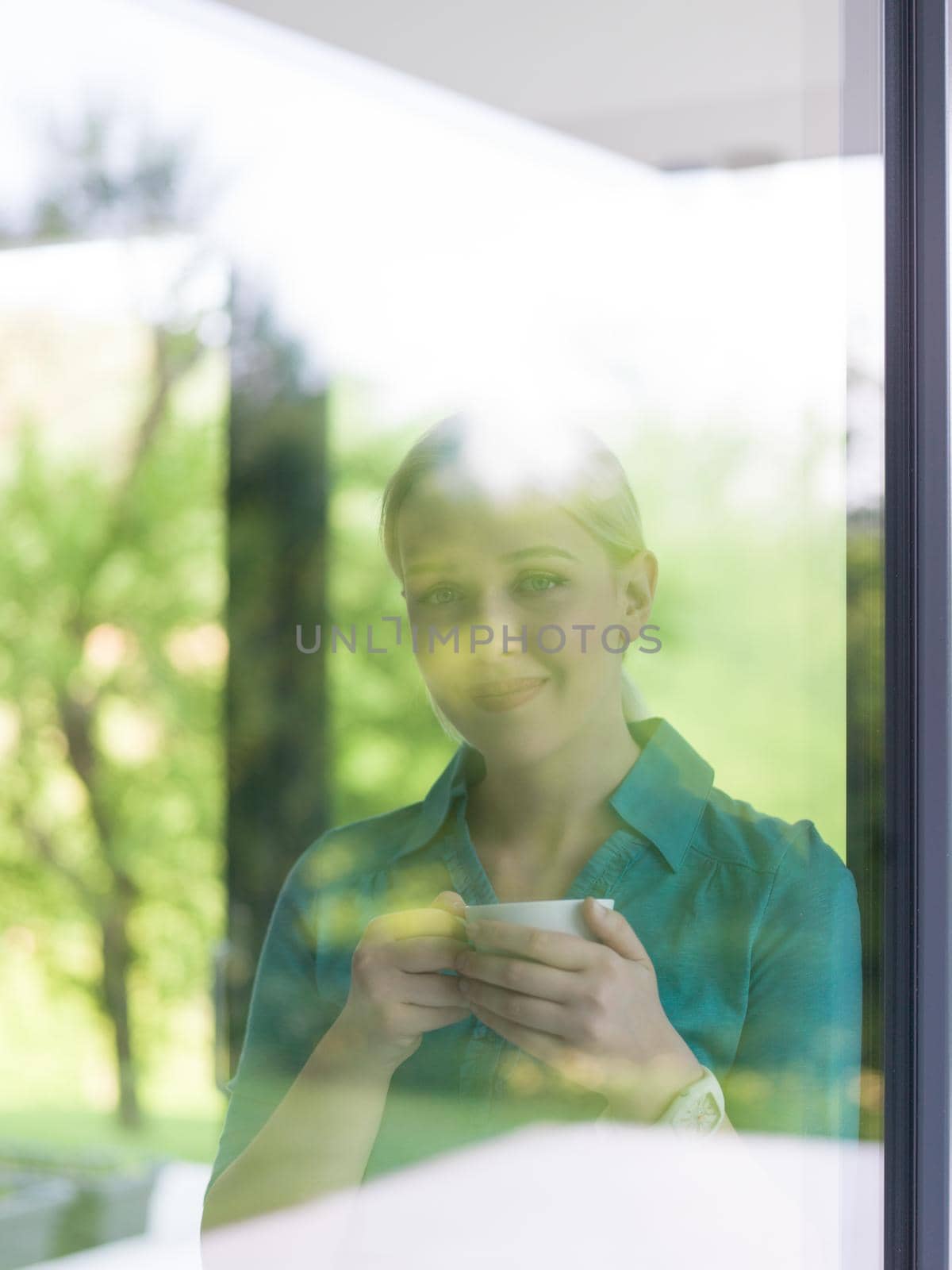 beautiful young woman drinking morning coffee by the window in her home