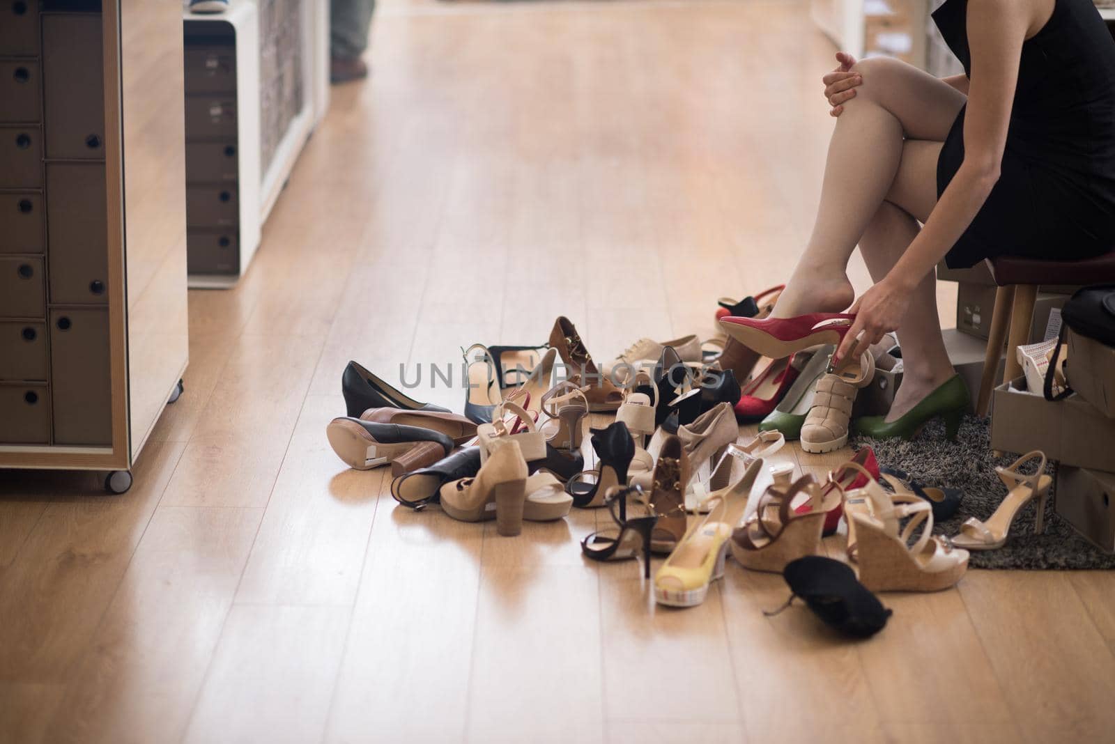 Hard choice. Close-up of young woman sitting in shoe store while different shoes laying near her