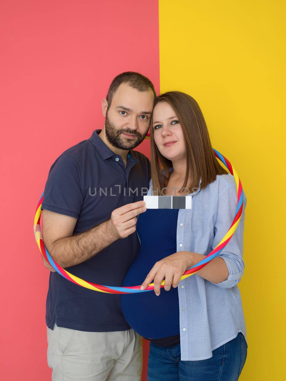 Portrait of a happy young couple,man holding his pregnant wife belly isolated over colorful background