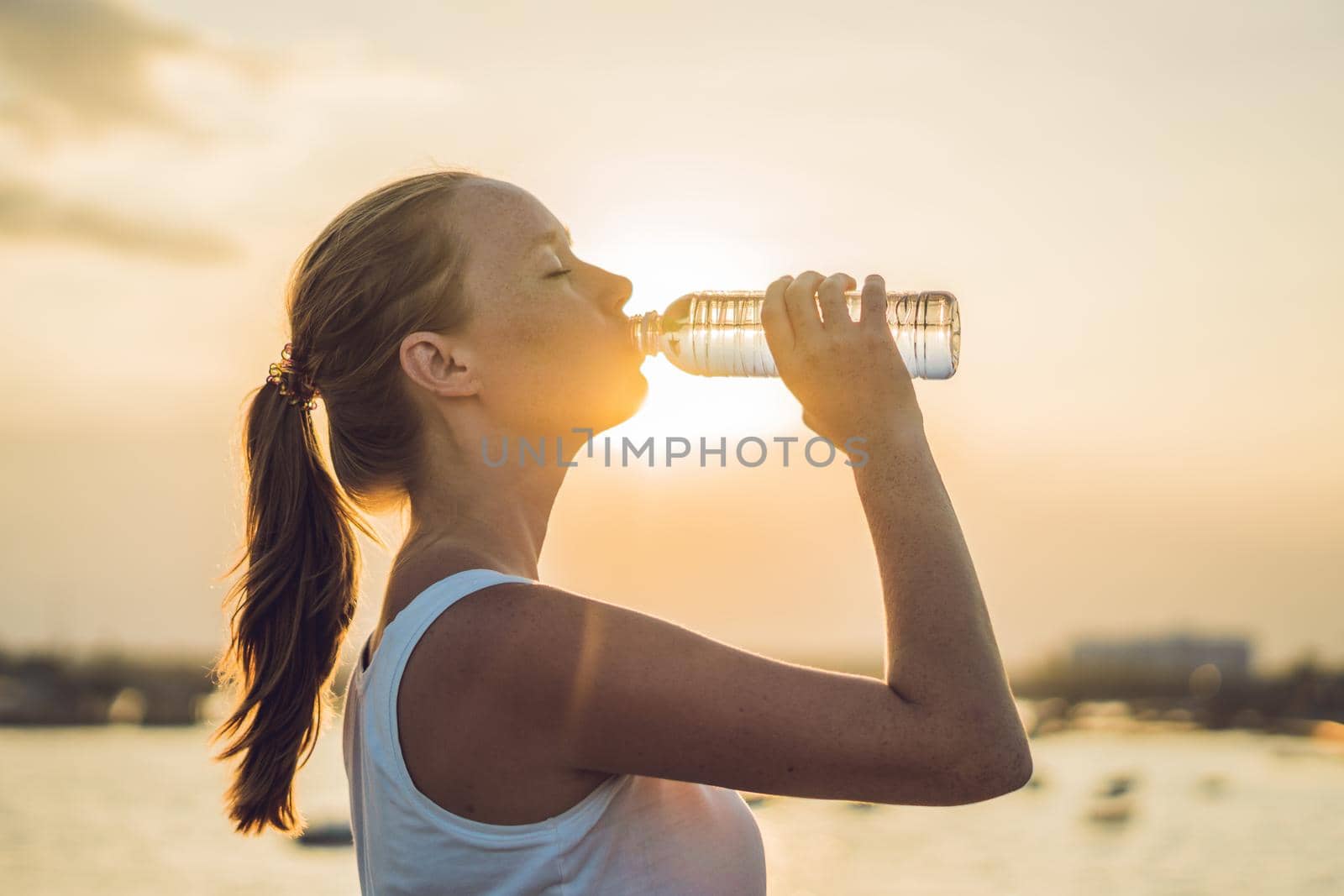 Sporty woman drinking water outdoor on sunny day.
