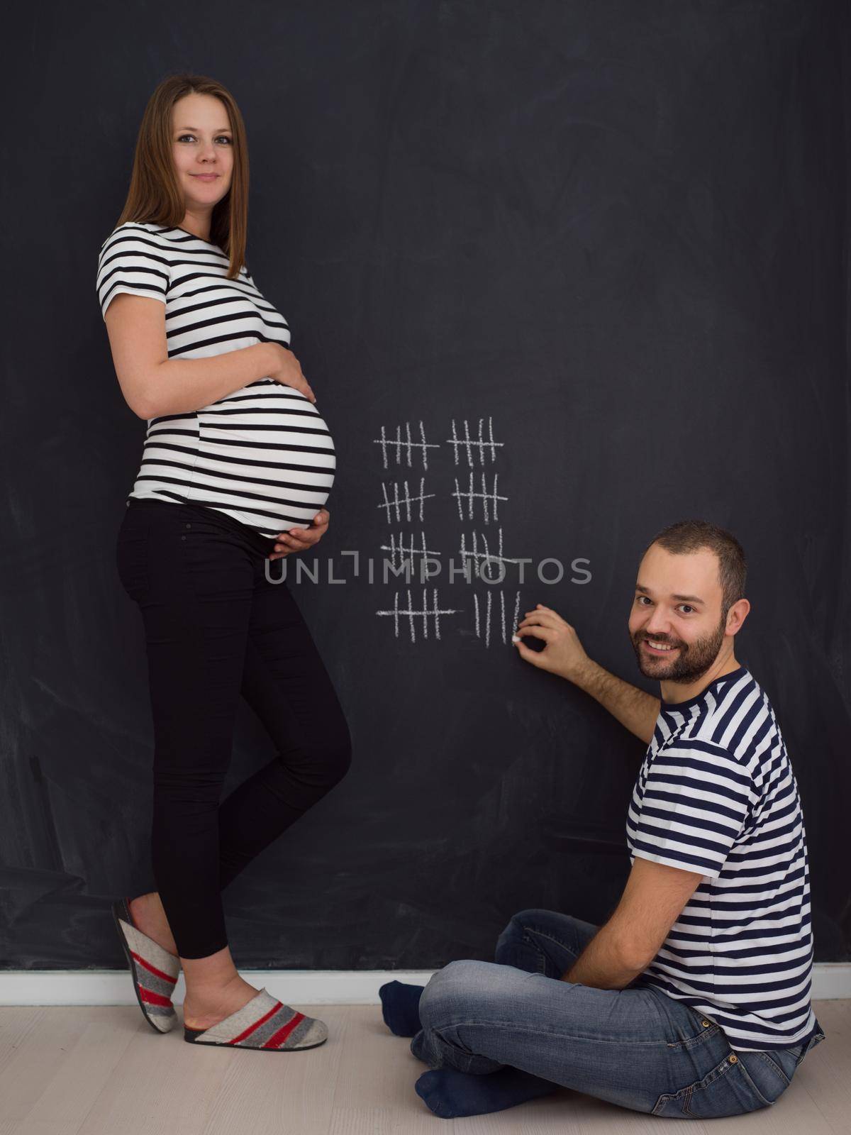 young pregnant couple accounts week of pregnancy and writing them with chalk on blackboard