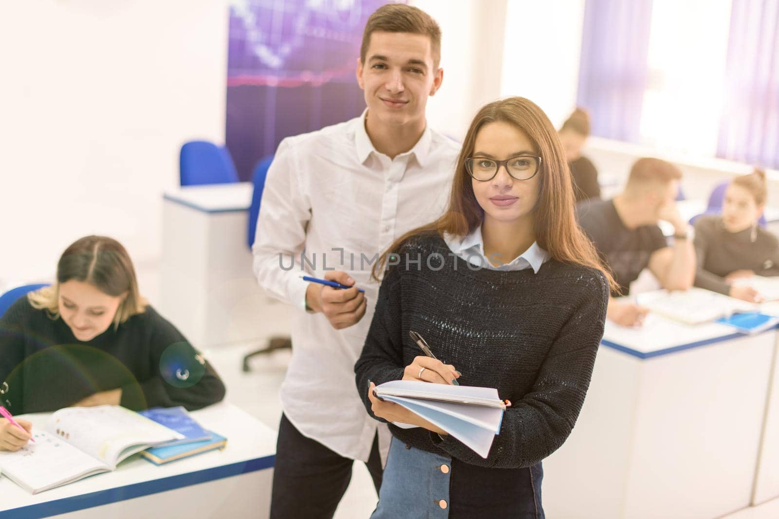 Two young students man and woman with others working on a project in a classroom writing notes  and discussing