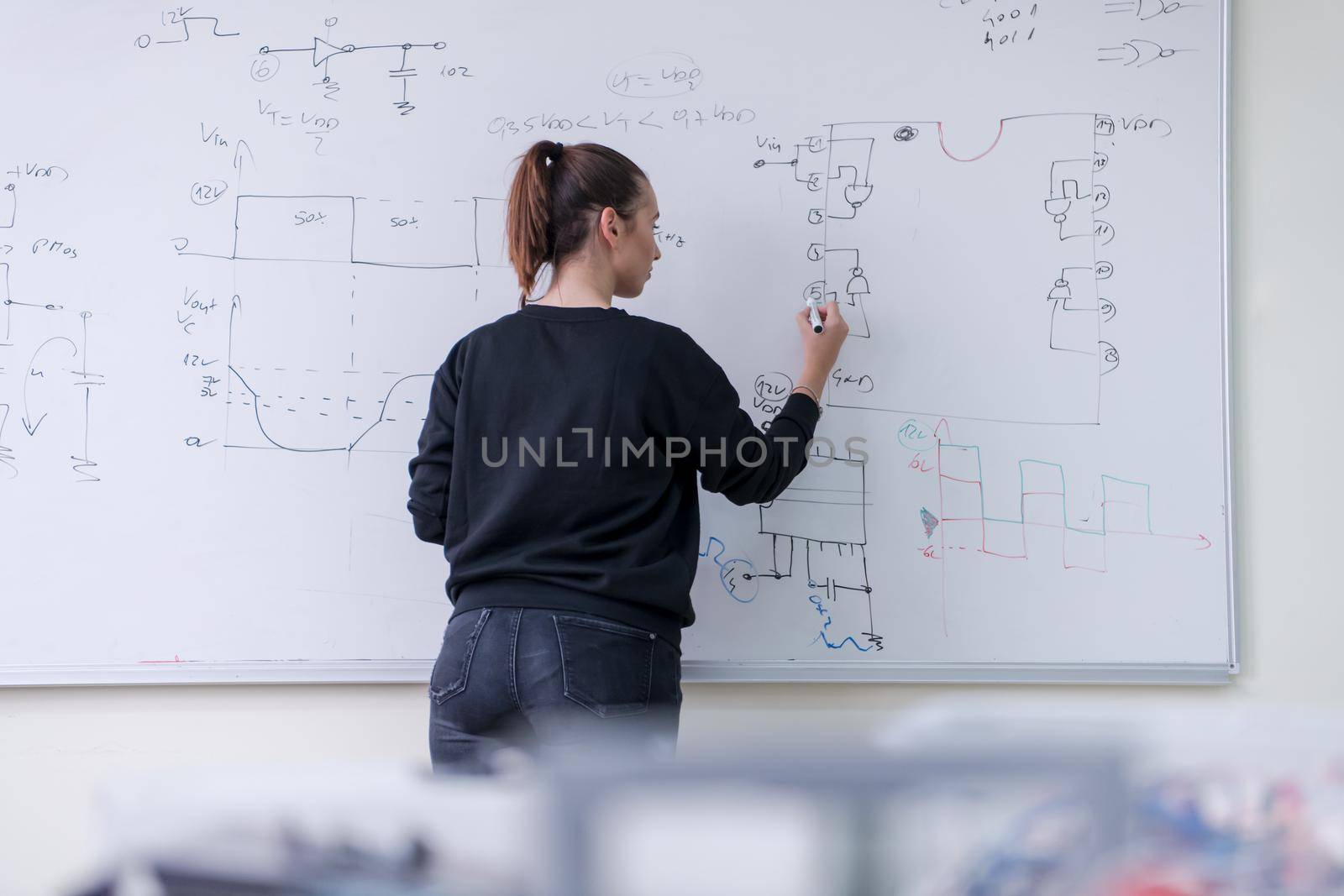 female student writing on board in classroom by dotshock