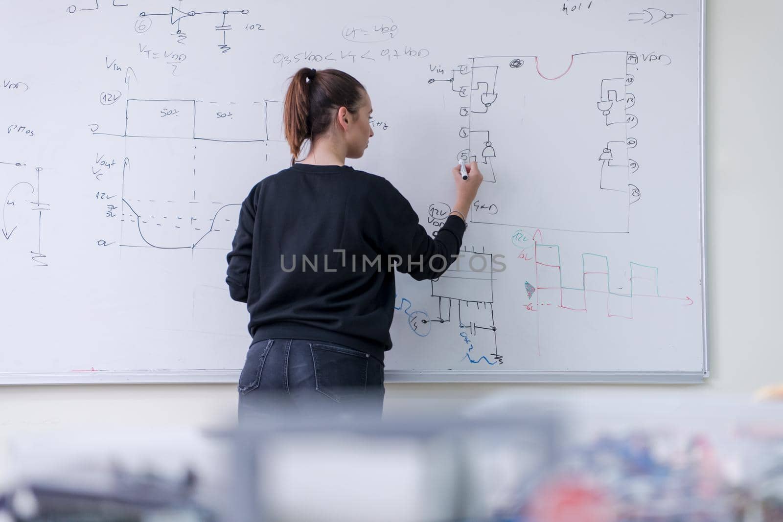 Young female student standing and writing on white chalkboard in a classroom
