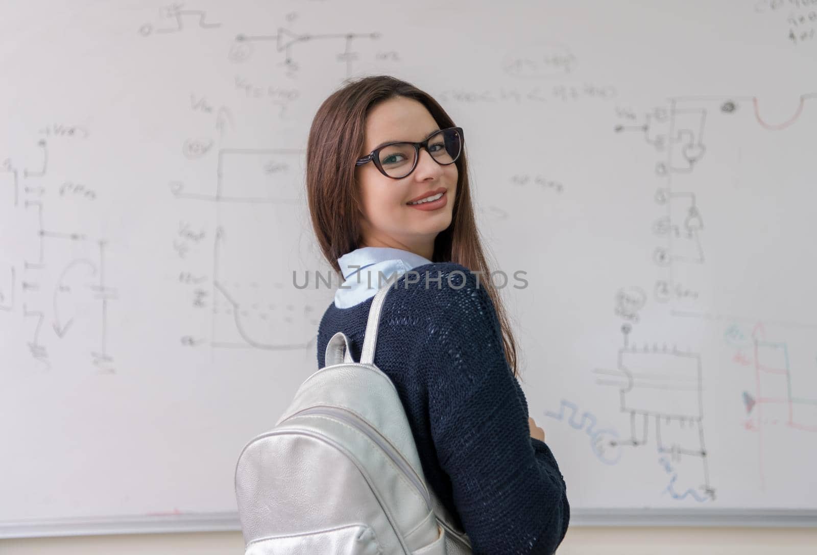 portrait of a young beautiful female student standing in front of white chalkboard and looking at the camera