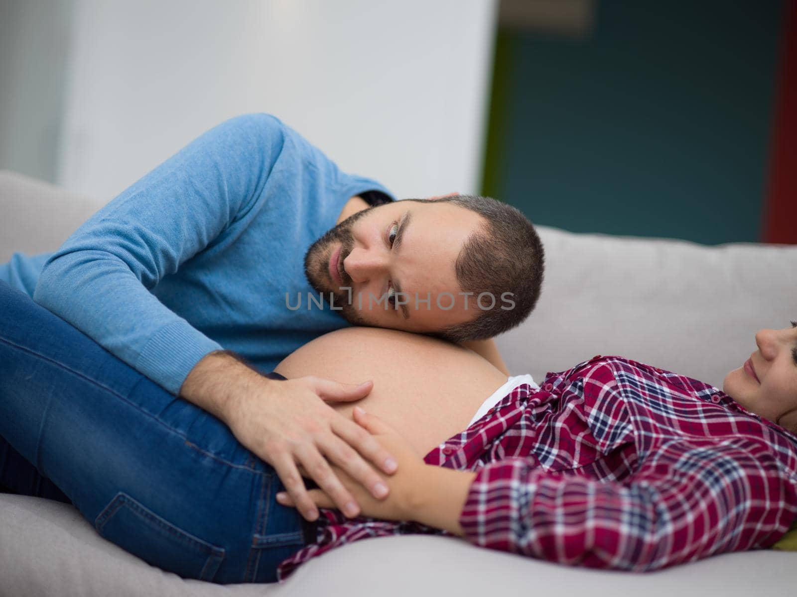 Happy future dad listening the belly of his pregnant wife while relaxing on sofa at home