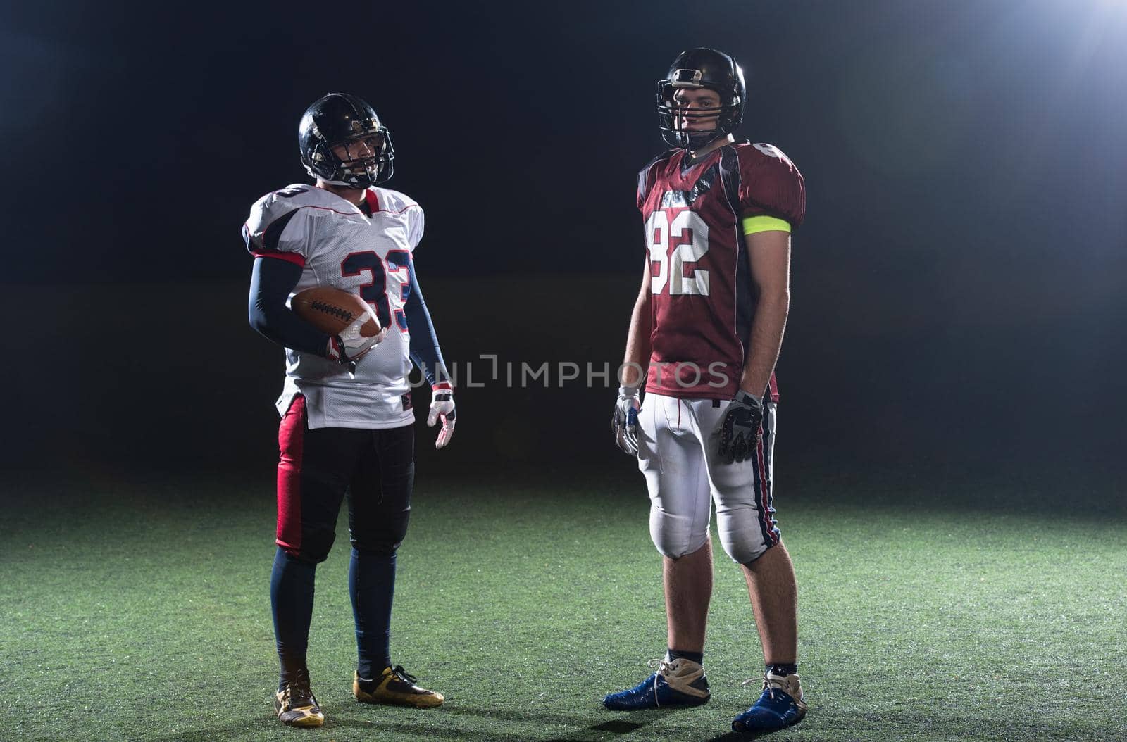 portrait of confident American football players holding ball while standing on field at night