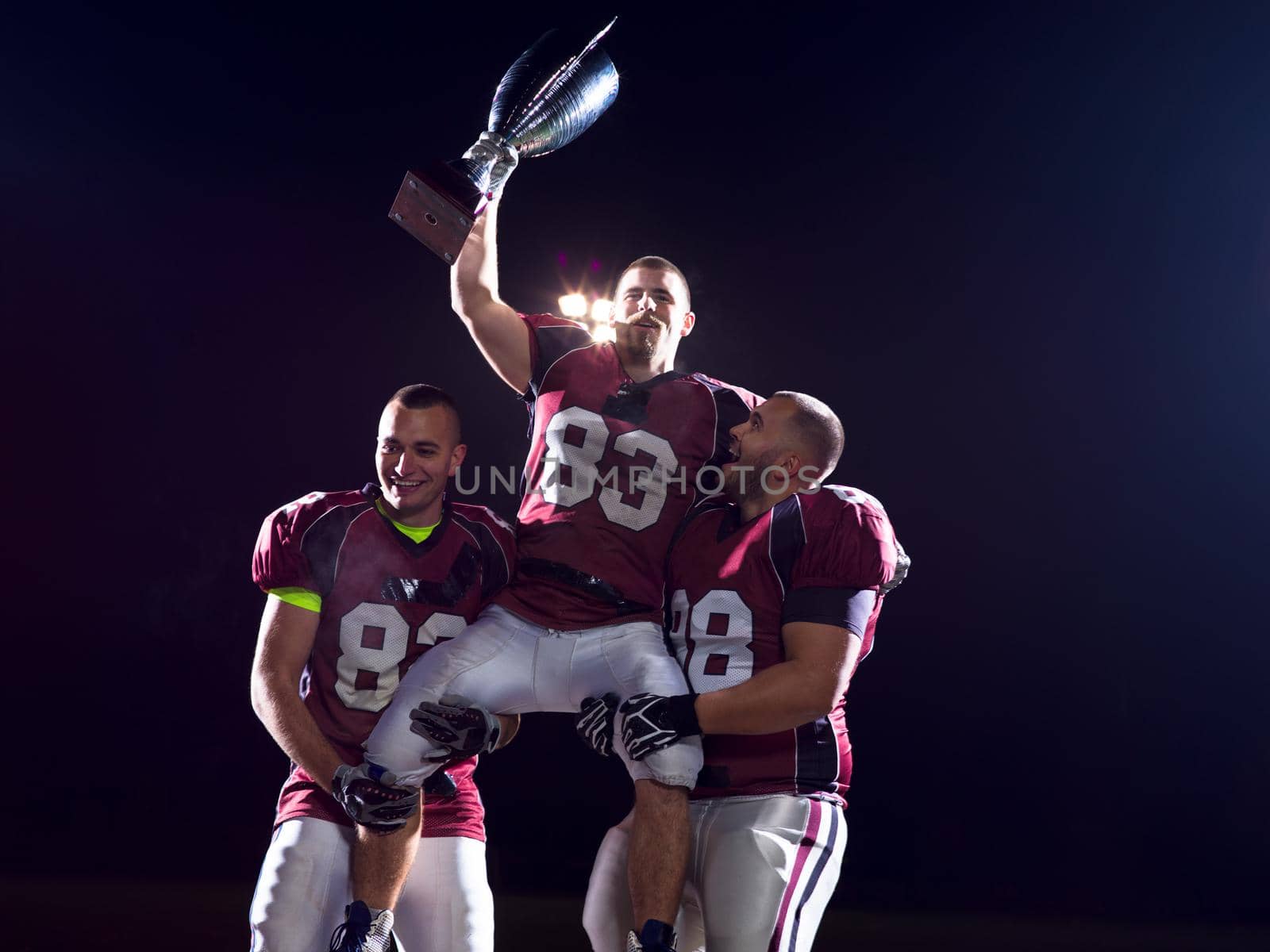 happy american football team with trophy celebrating victory on night field