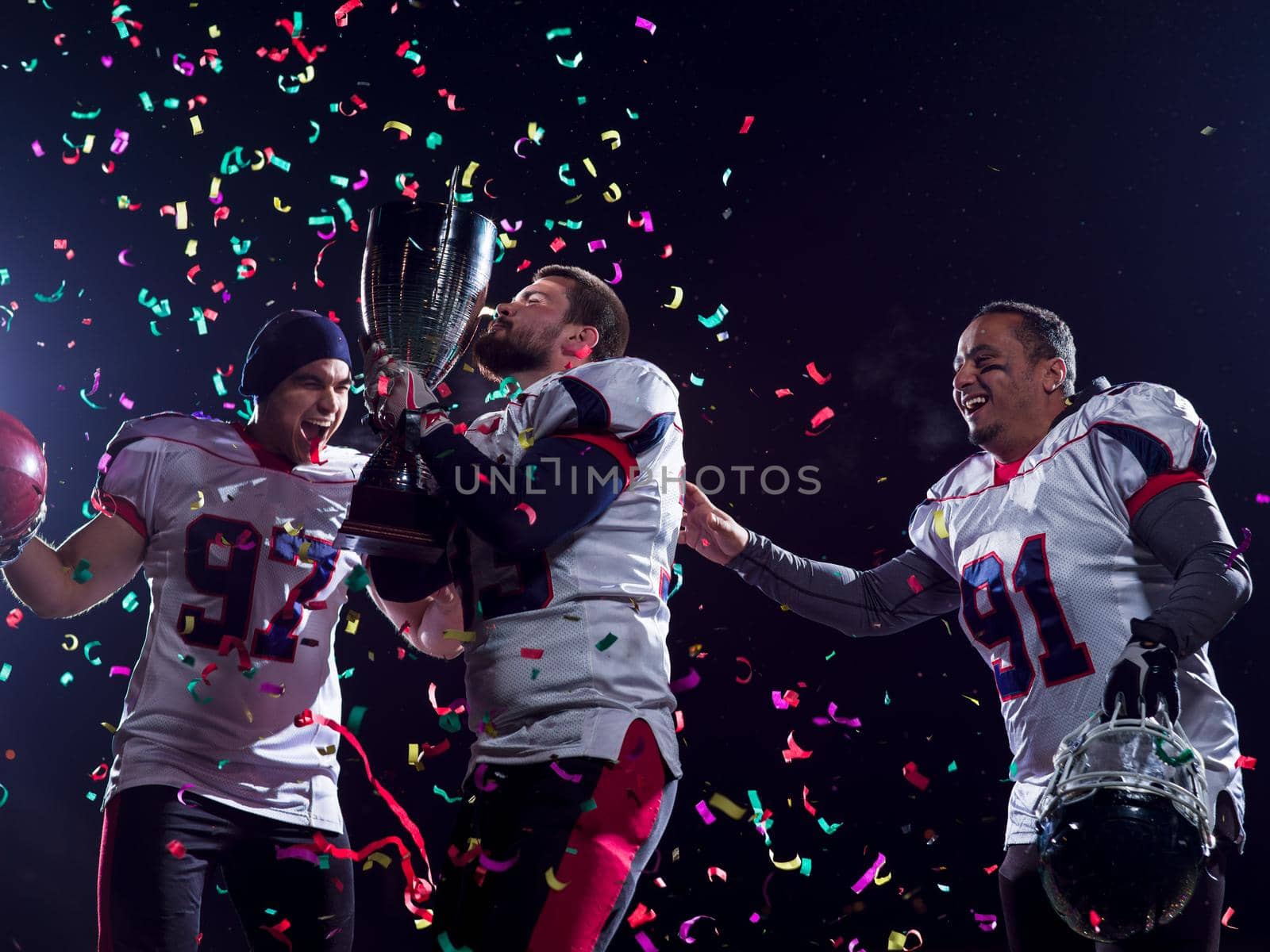 happy american football team celebrating victory with trophy and confetti on the night field