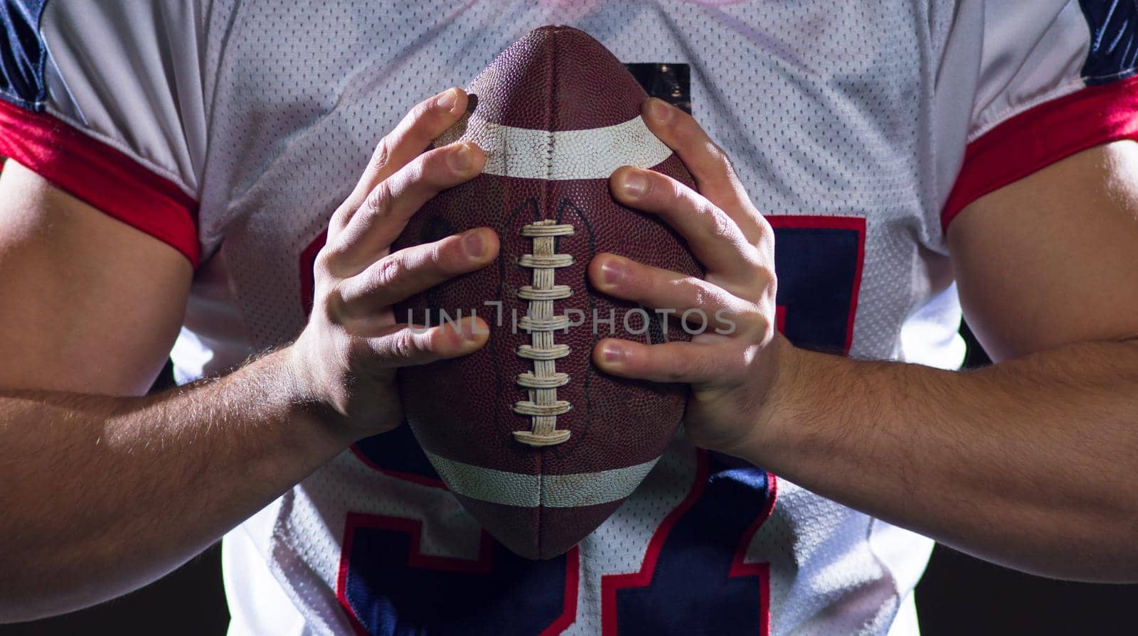 portrait of confident American football player holding ball while standing on field at night