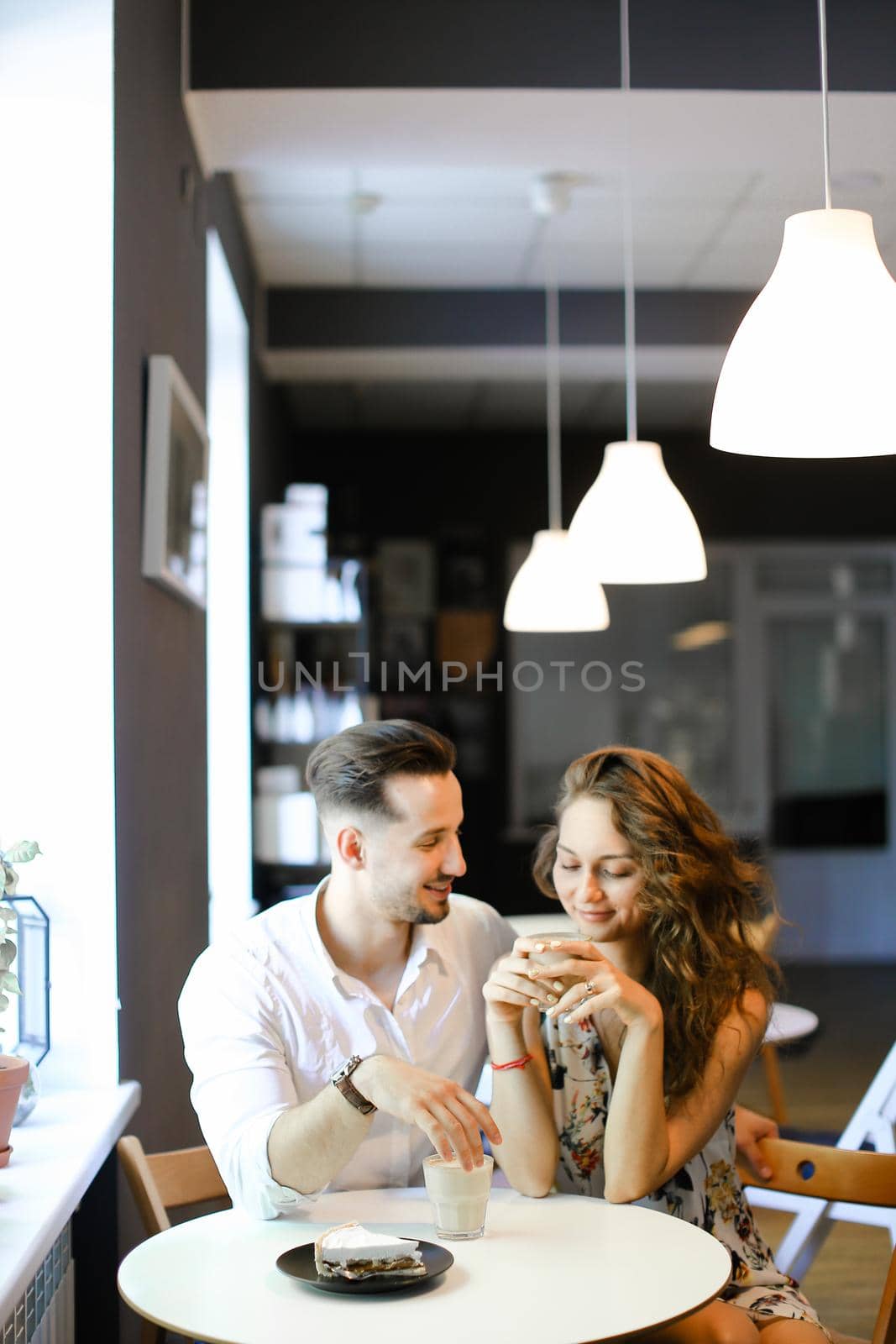 Young european husband hugging wife and sitting at cafe, drinking coffee. Concept of enjoing togetherness and having lunch.