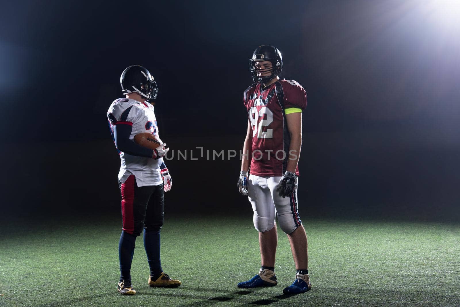 portrait of confident American football players holding ball while standing on field at night